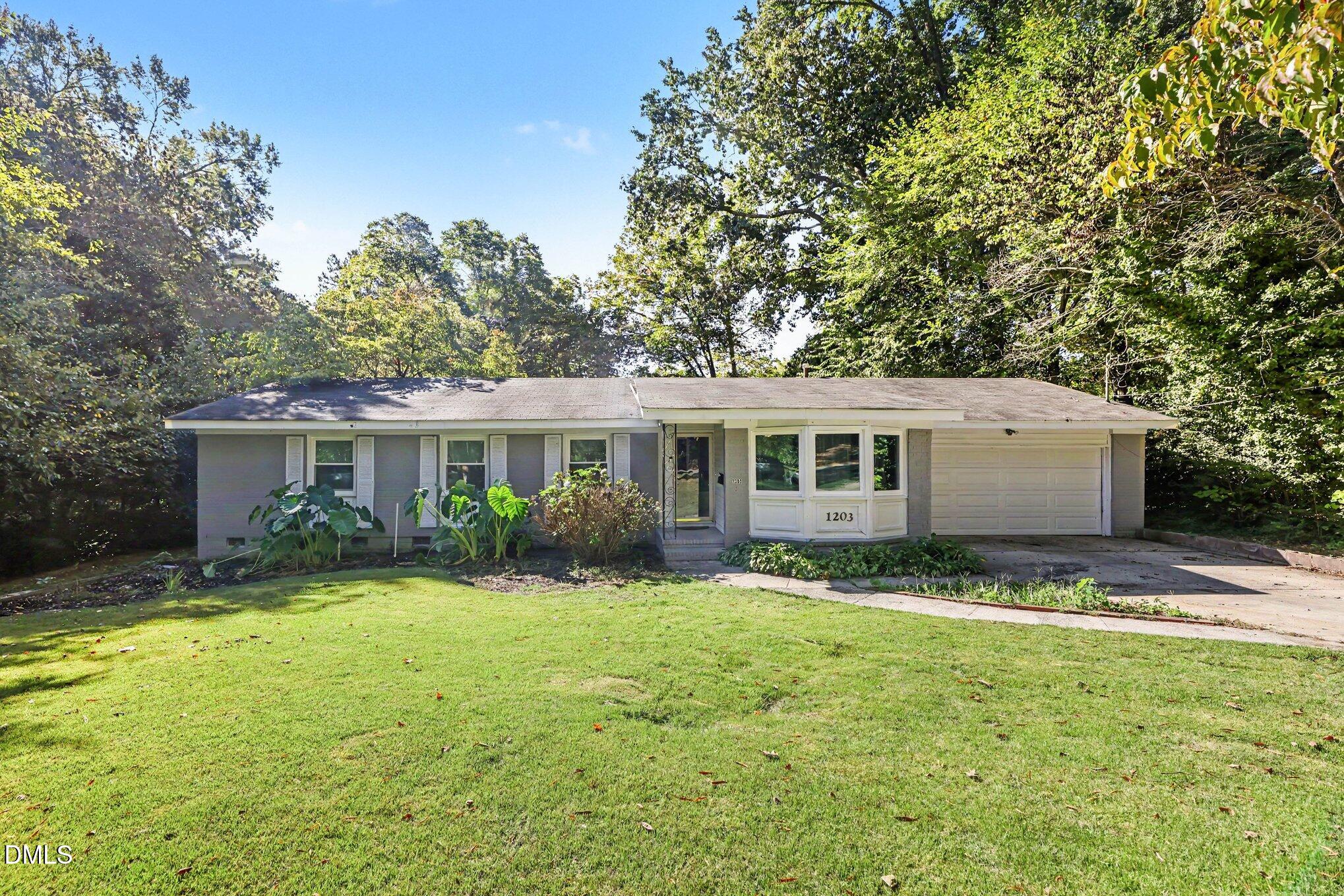 Single-story gray home with a white bay window, attached garage, and leafy landscaping.