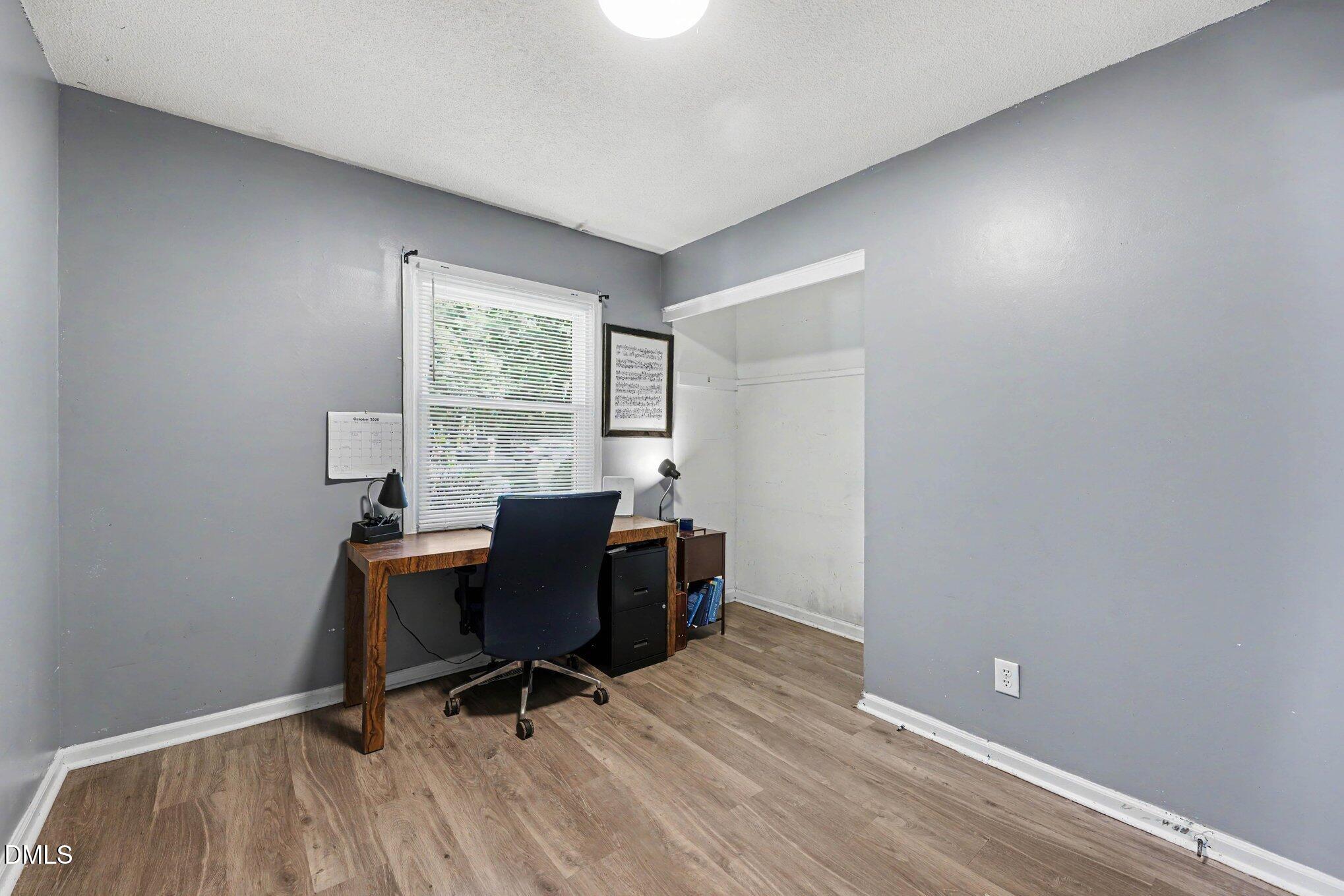 Home office with a wooden desk beneath a window with white blinds and a built-in alcove.