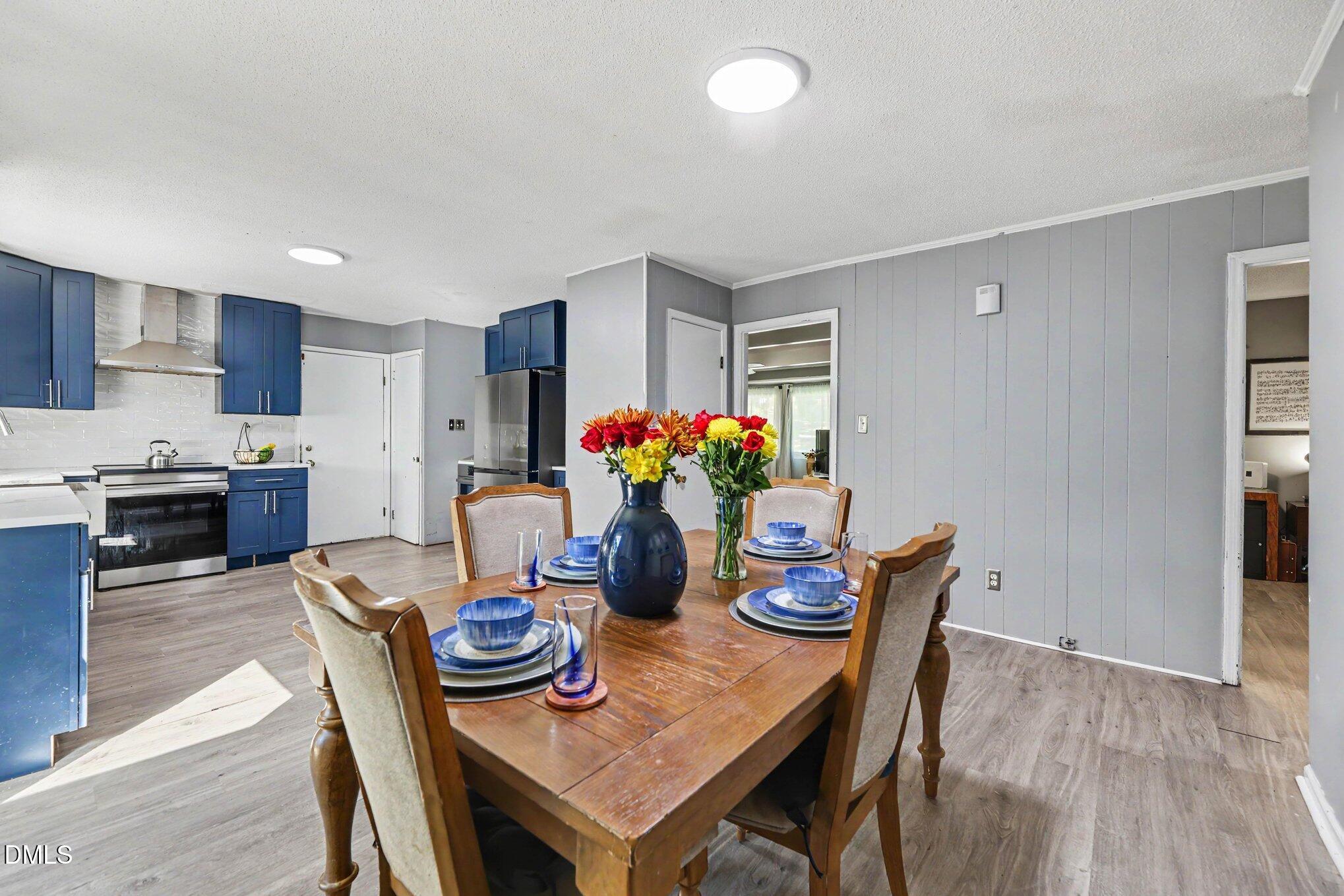 Open kitchen and dining area with blue cabinets, stainless appliances, and a flower centerpiece on the table.