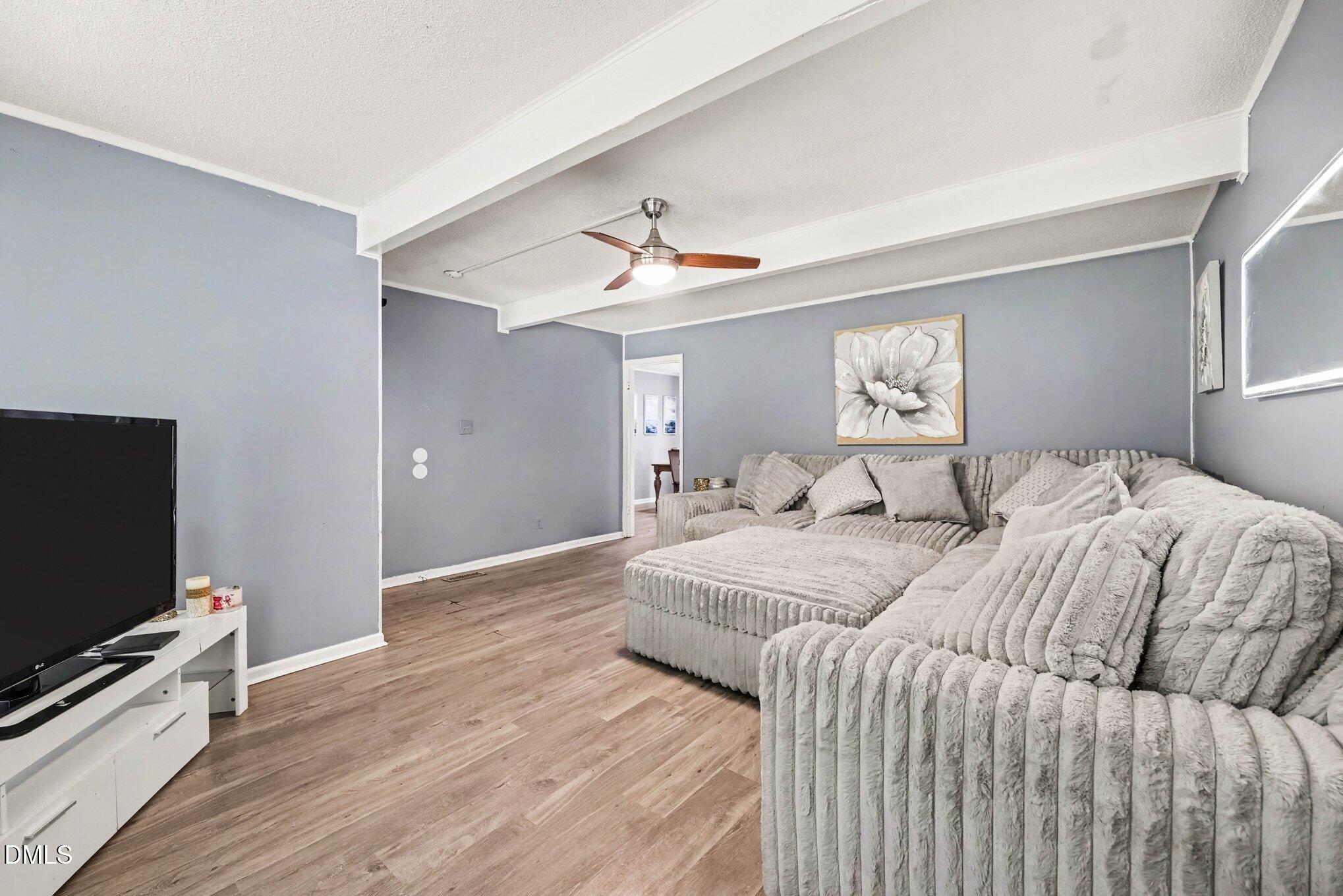 Living room with a plush gray sectional, wood-look flooring, and exposed ceiling beams.