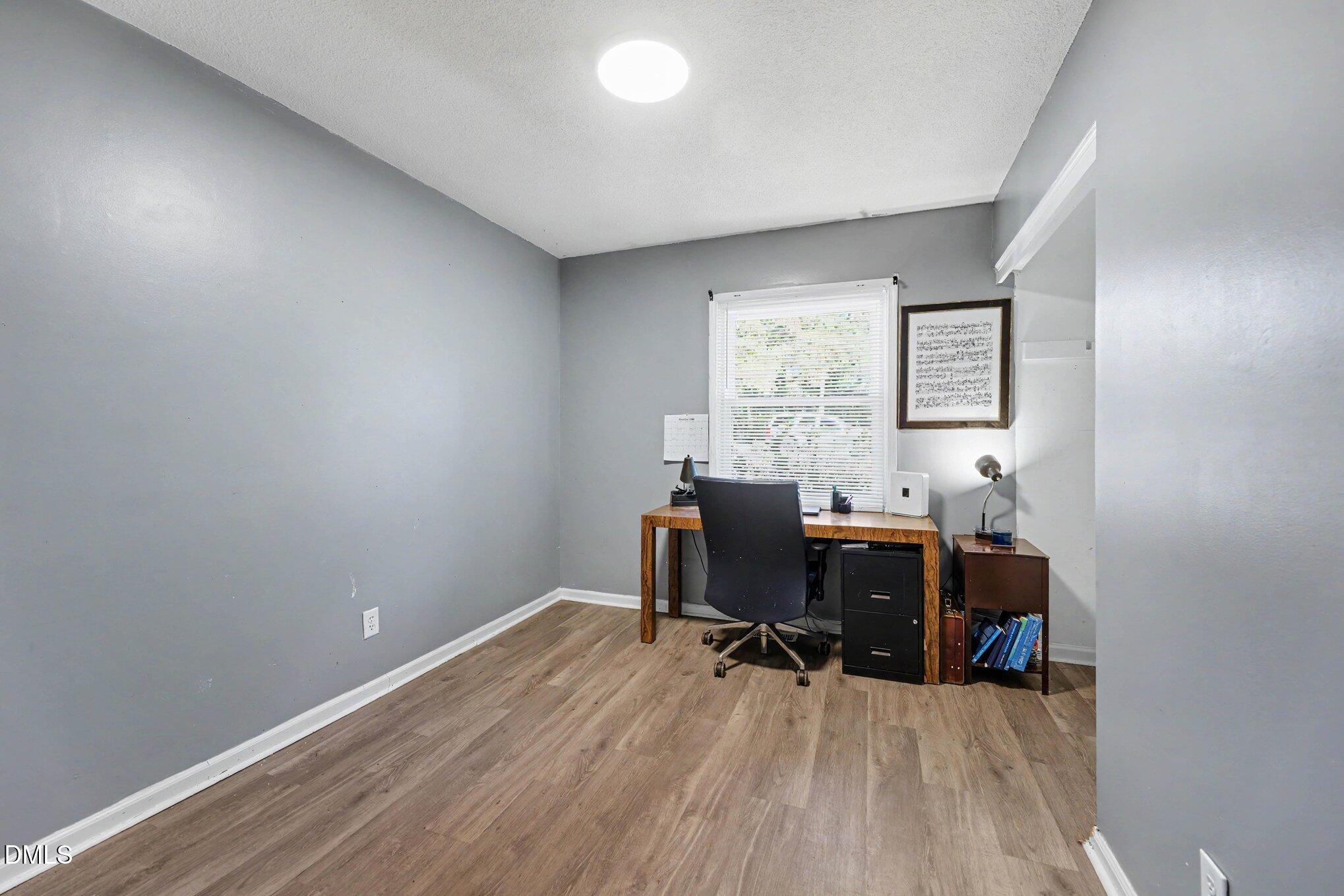 Home office with a wooden desk beneath a window and gray walls.