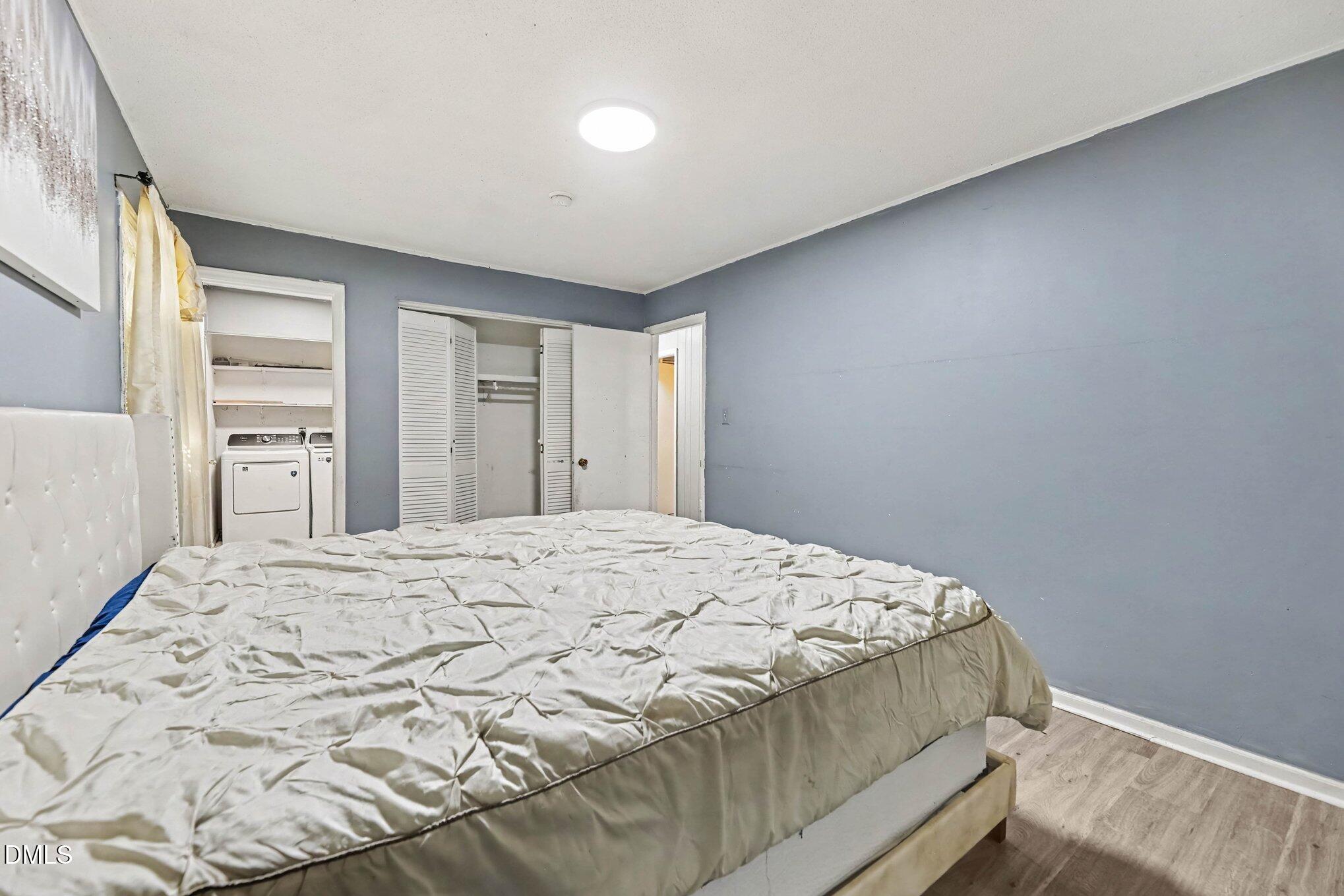 Bedroom with a large bed, gray-blue walls, and an open closet beside a laundry area.