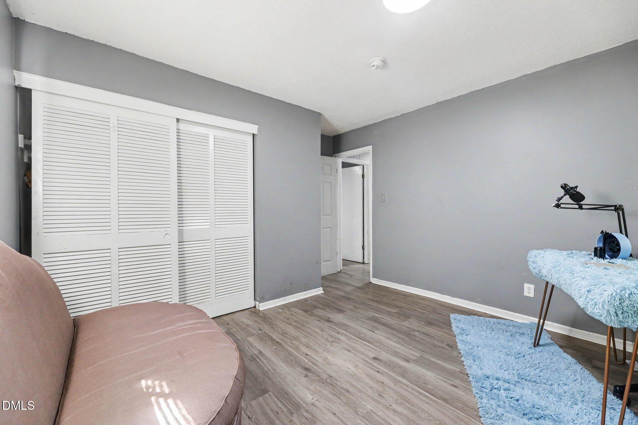 Gray room with louvered closet doors, a pink sofa, blue rugs, and a microphone setup.