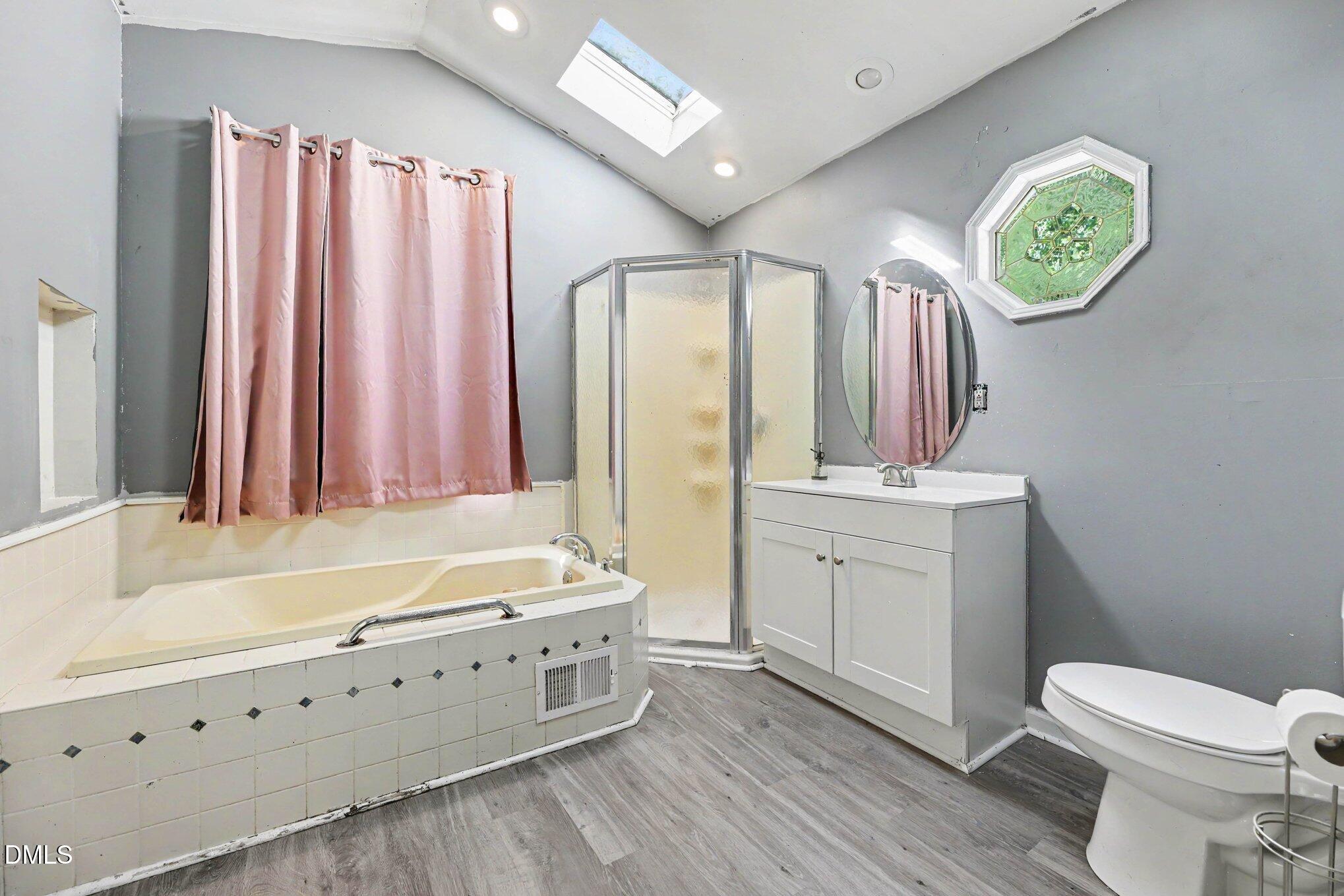 Bathroom with a corner shower, soaking tub, skylight, and pink curtains.