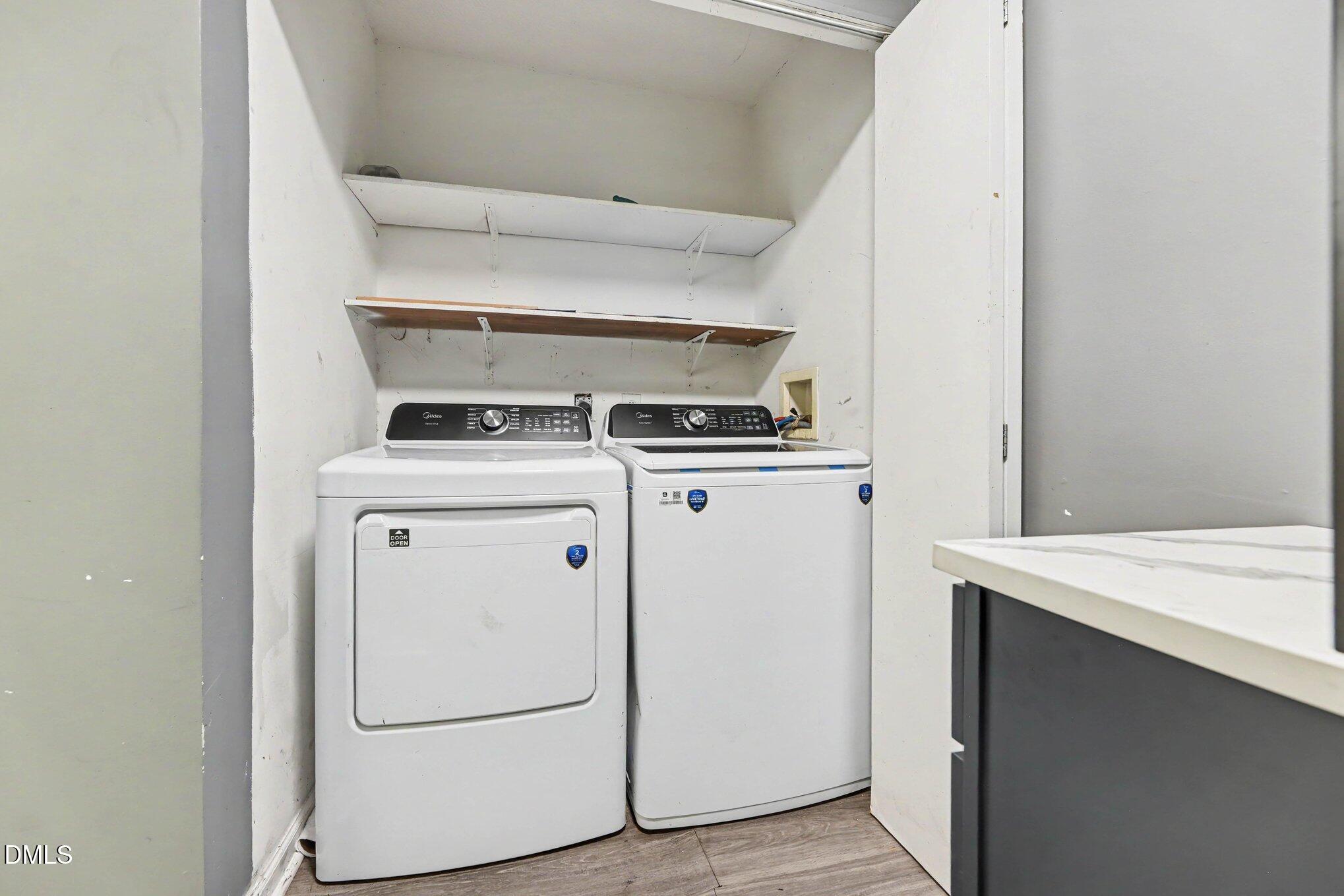 Laundry room with a front-loading dryer, top-loading washer, and open wall shelves.