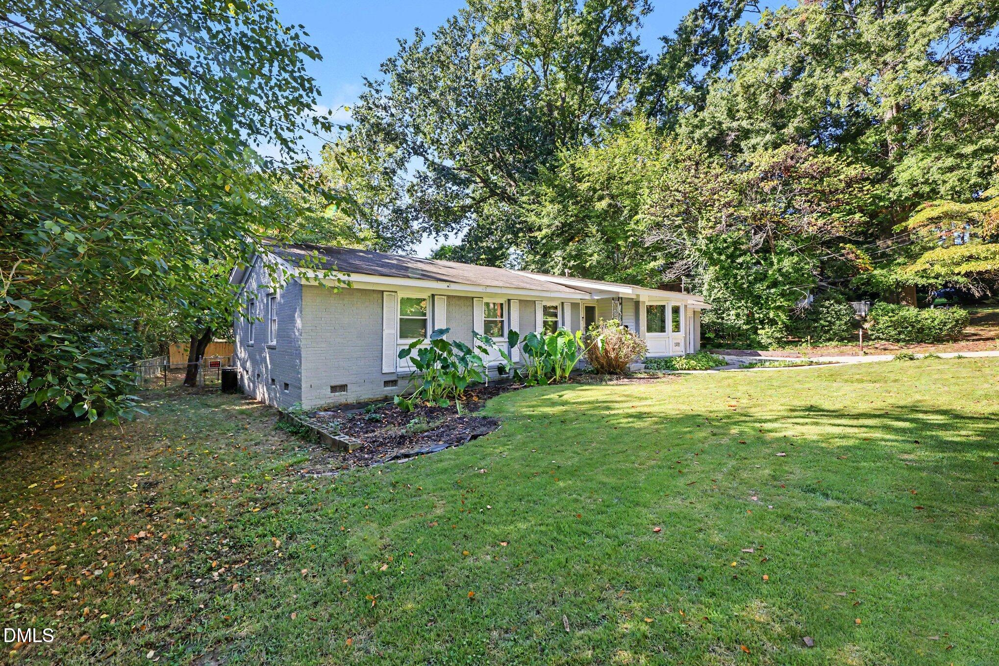 Single-story brick ranch home surrounded by mature trees and a broad green lawn.