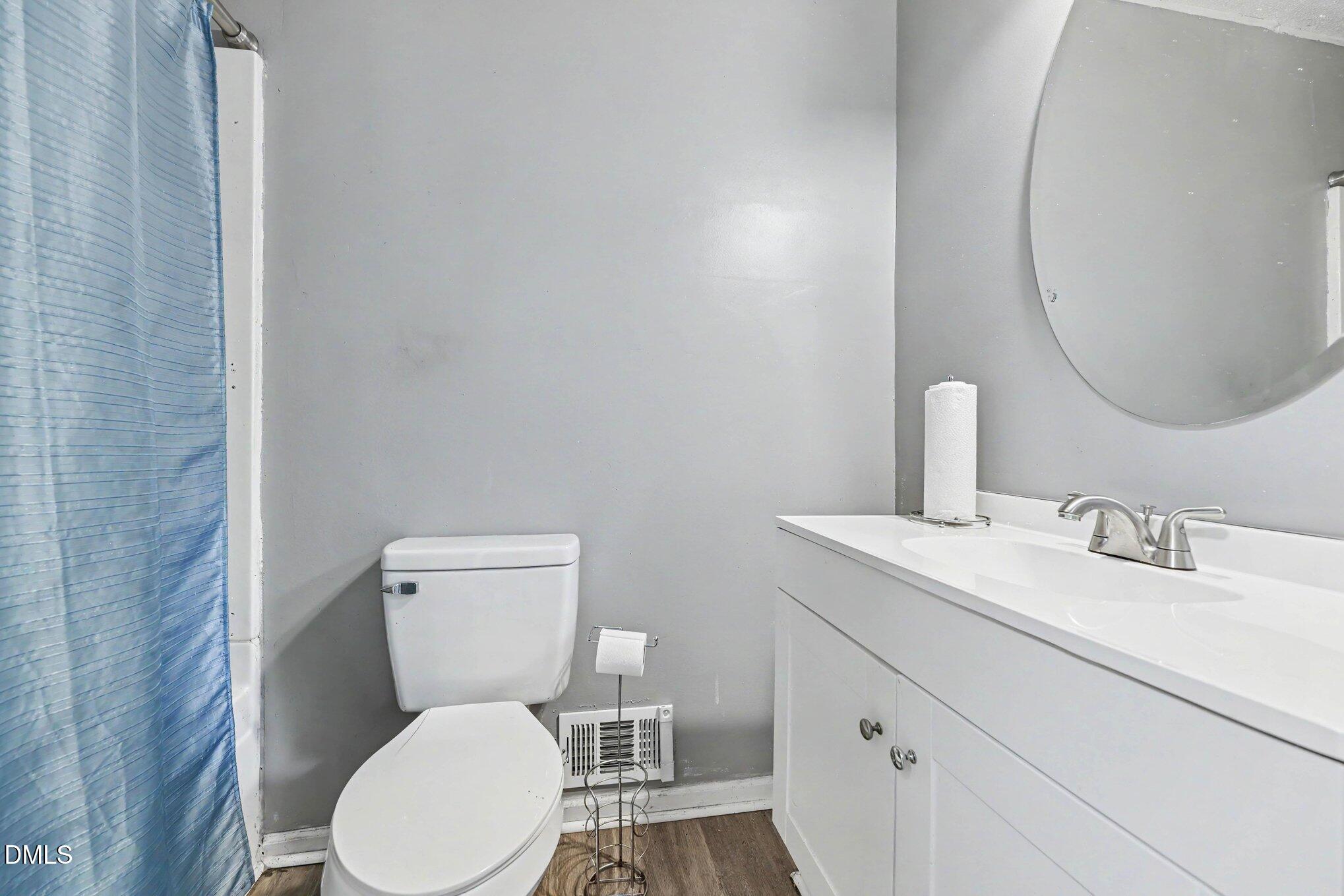 Bathroom with a blue shower curtain, white vanity, round mirror, and toilet.