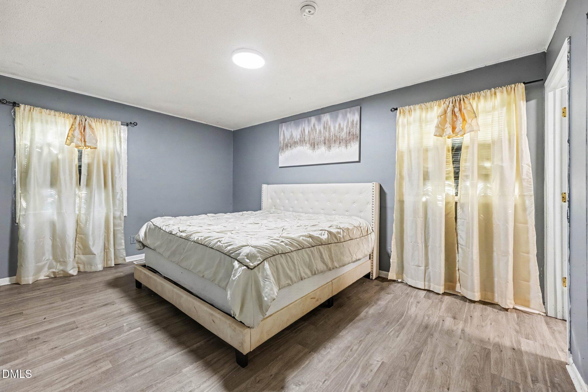 Bedroom with a white upholstered bed, gray walls, and cream curtains over two windows.