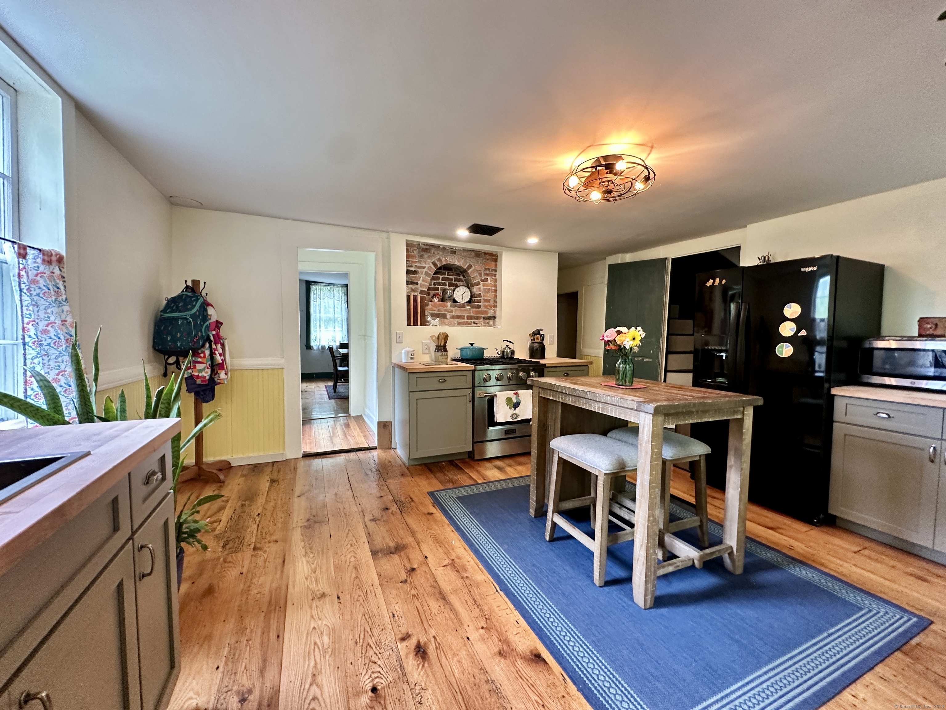 Kitchen with wood floors, green-gray cabinets, stainless range, and a rustic island table on a blue rug.