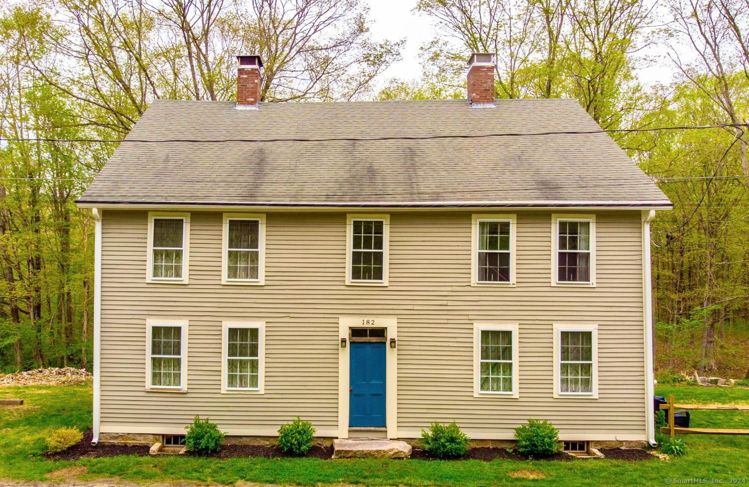 Two-story beige house with a steep roof, brick chimneys, and a bright blue front door.
