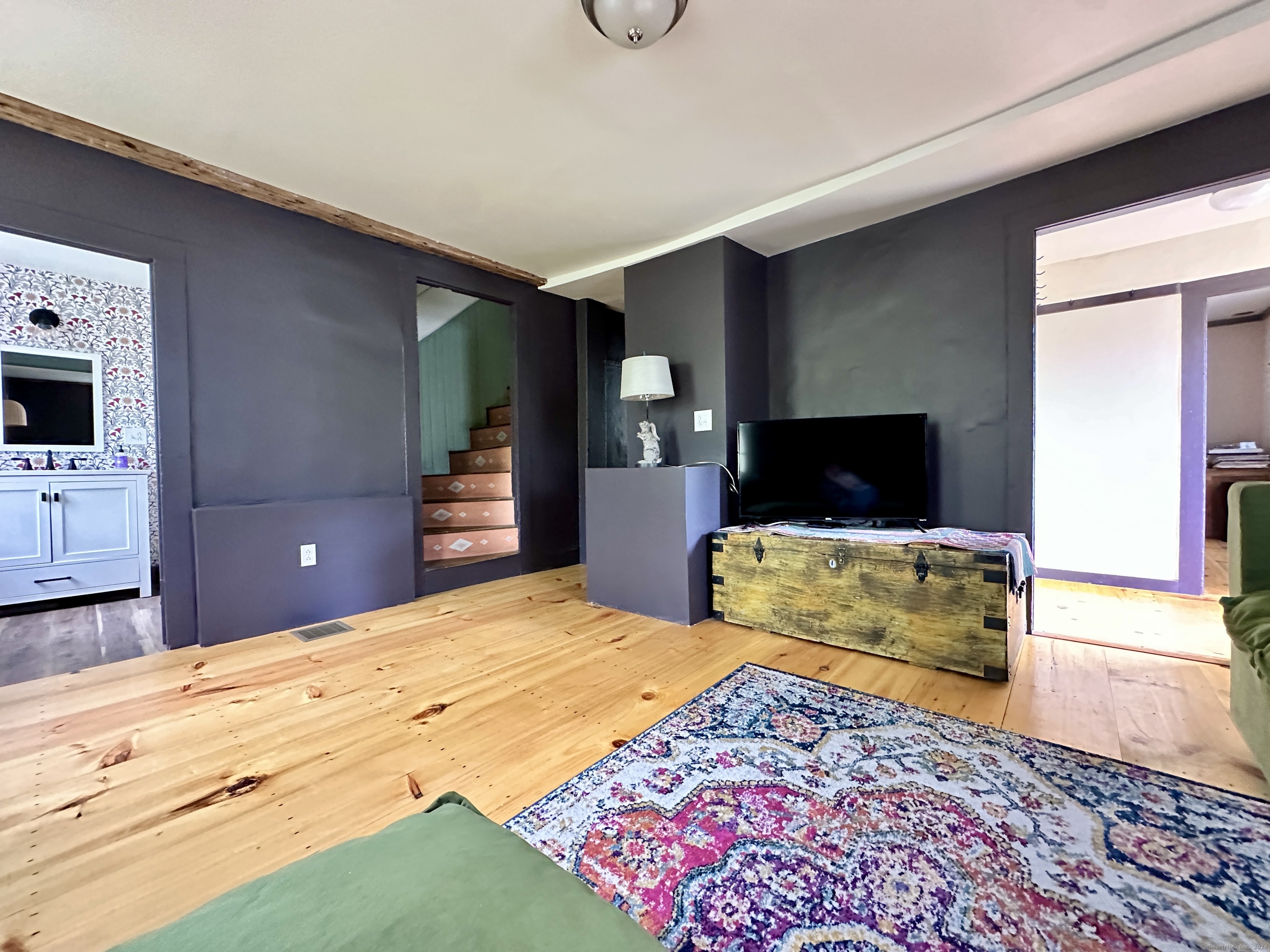 Living room with dark walls, wide plank floors, a staircase, and a television on a wooden trunk.