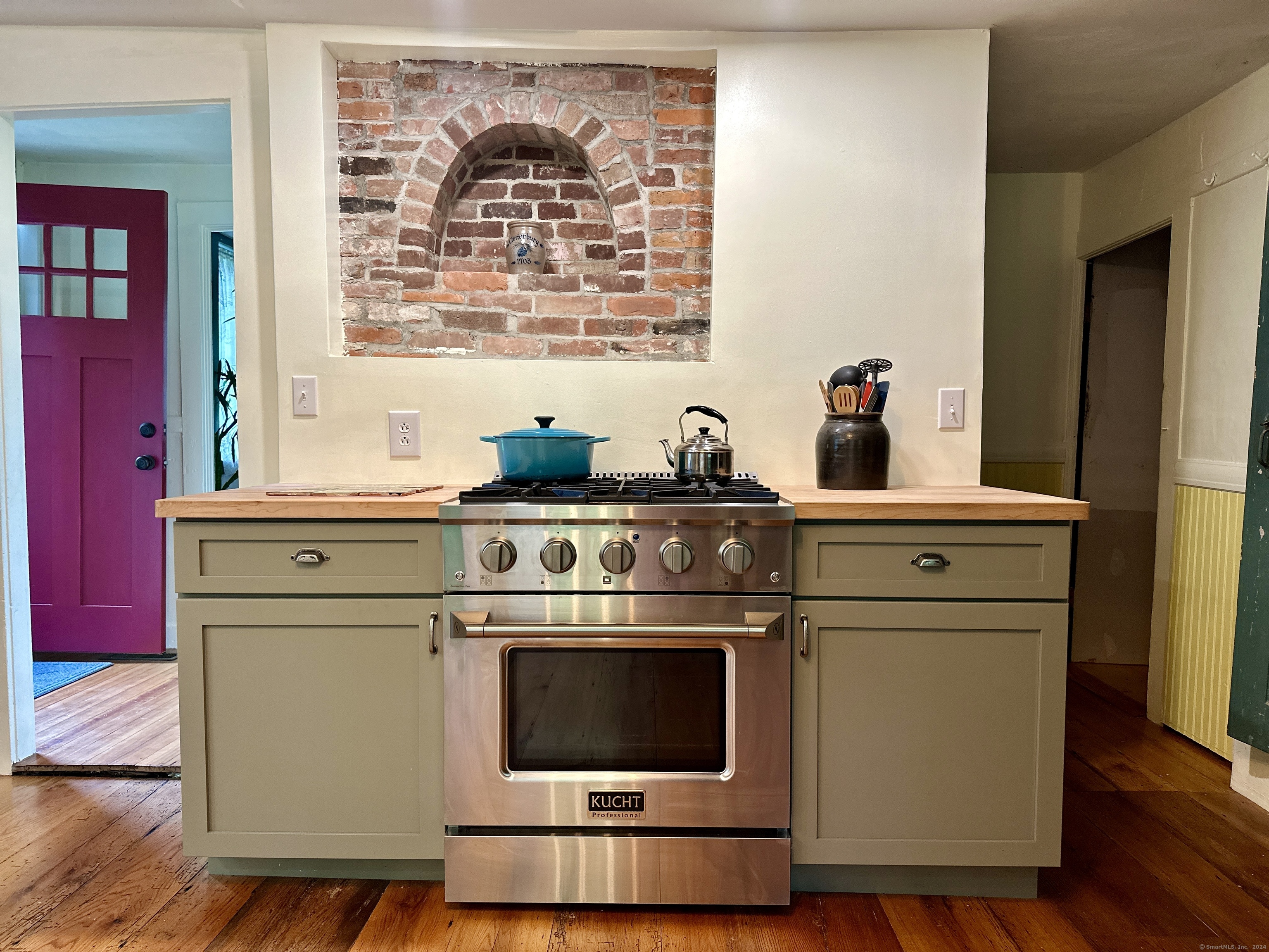 Kitchen with a stainless-steel range, sage-green cabinets, butcher-block counter, and arched brick alcove.