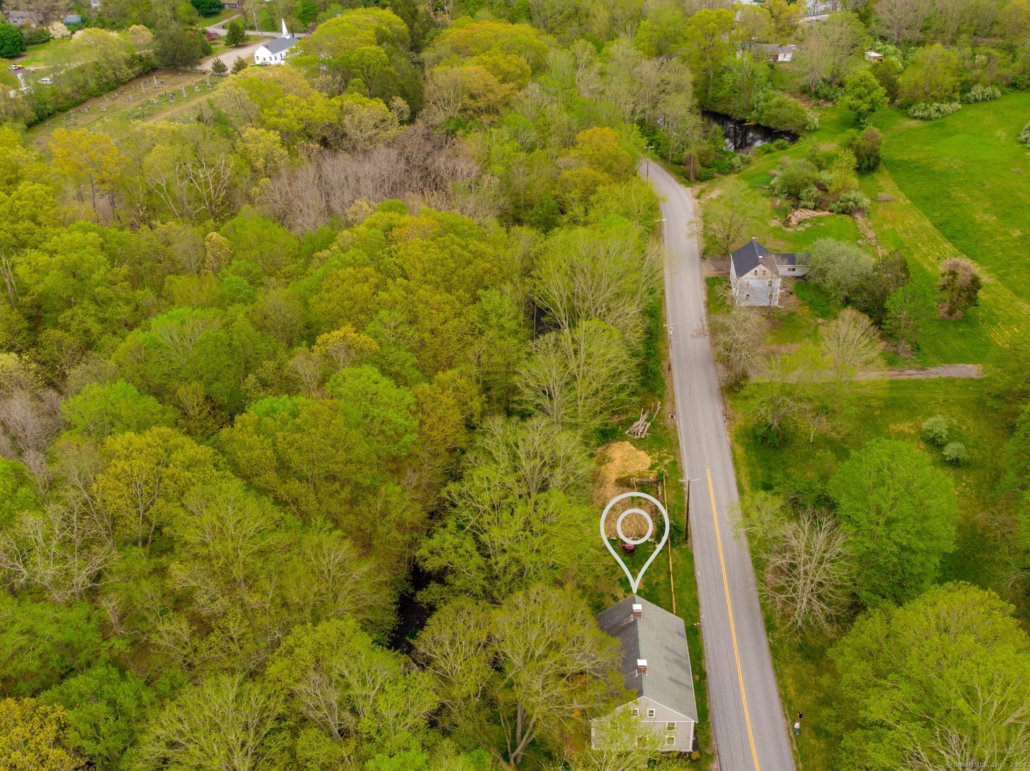 Aerial view of a house beside a road, marked by a pin and surrounded by woods and a stream.