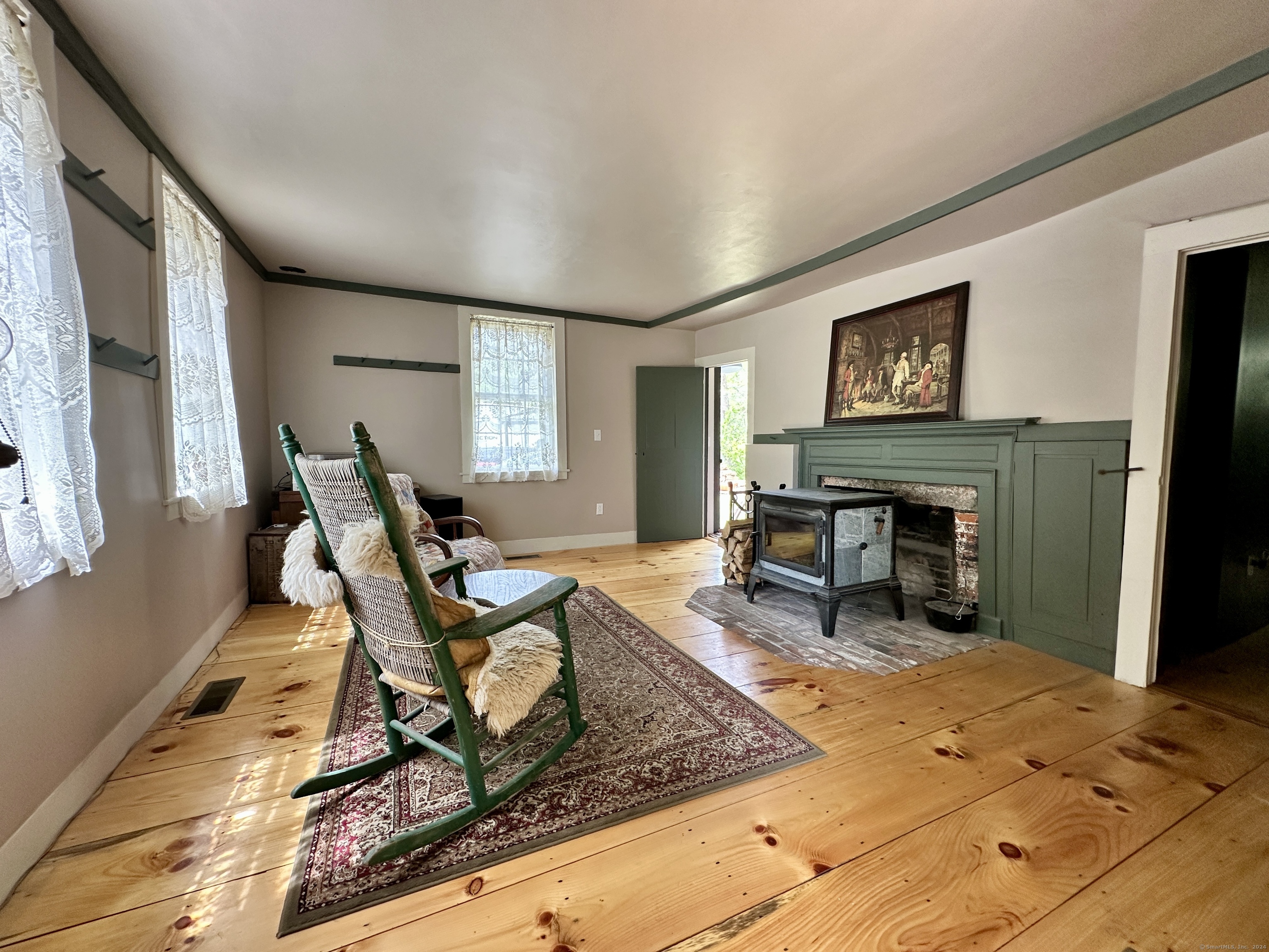 Living room with pine floors, a green fireplace and wood stove, and green rocking chairs.