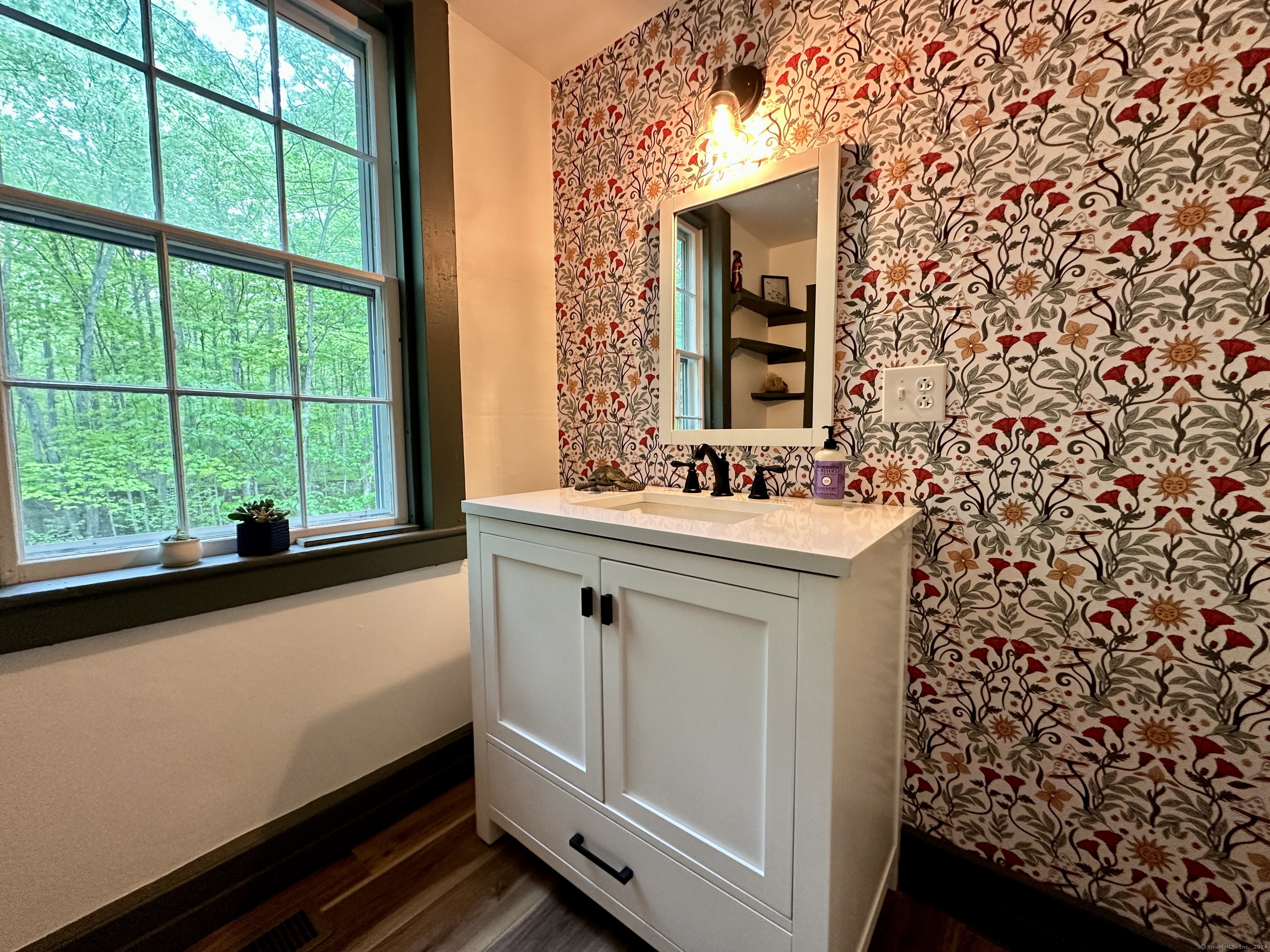 Bathroom vanity beside a large window, with bold floral wallpaper and trees outside.
