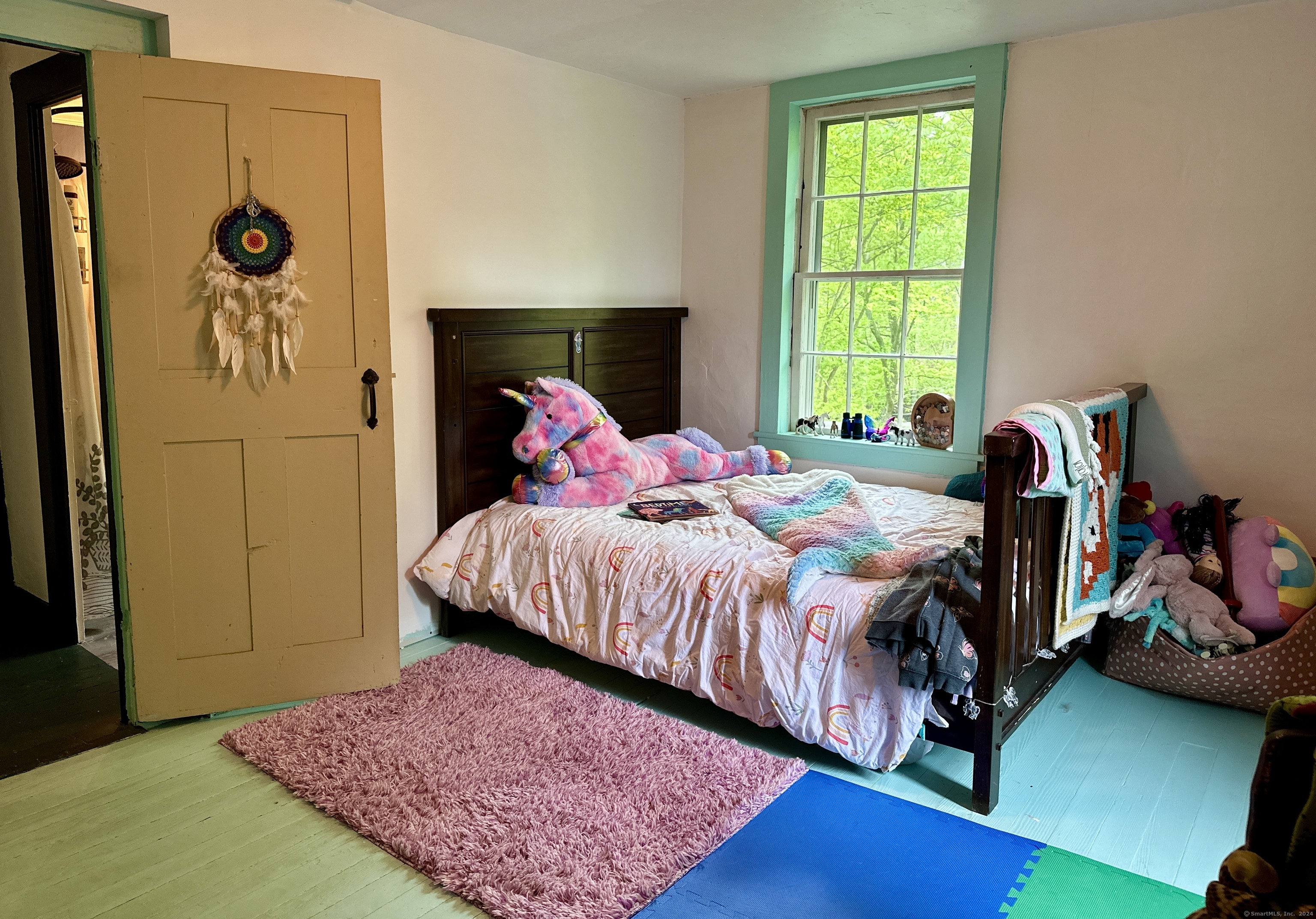 Child’s bedroom with a colorful unicorn plush toy on a dark wooden bed beside a tall window.