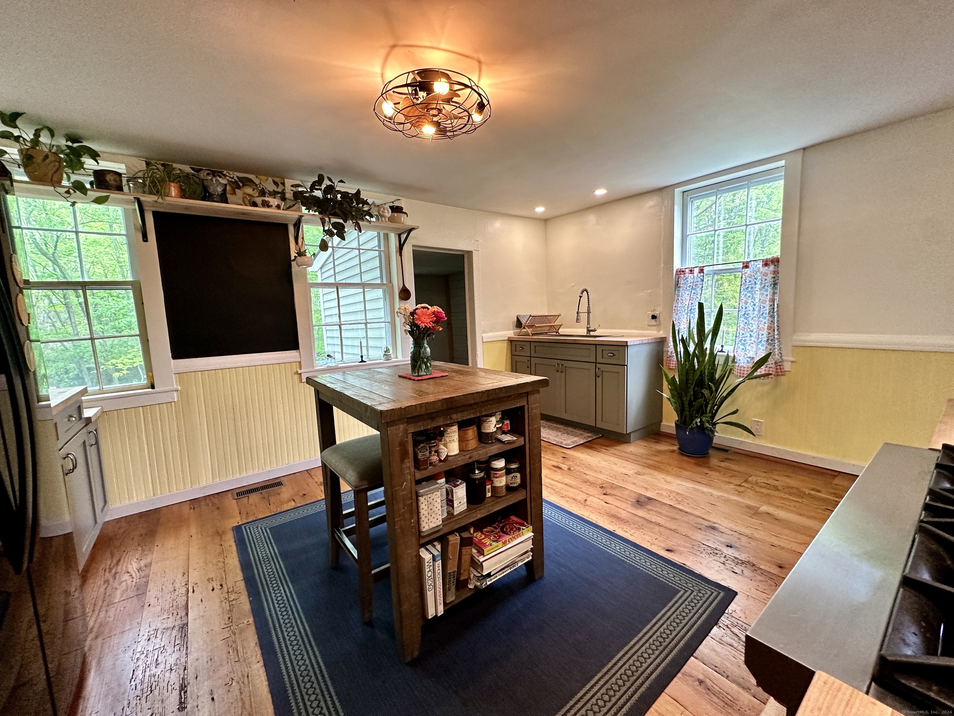 Kitchen with a rustic wooden island, wide-plank floors, and windows overlooking leafy trees.