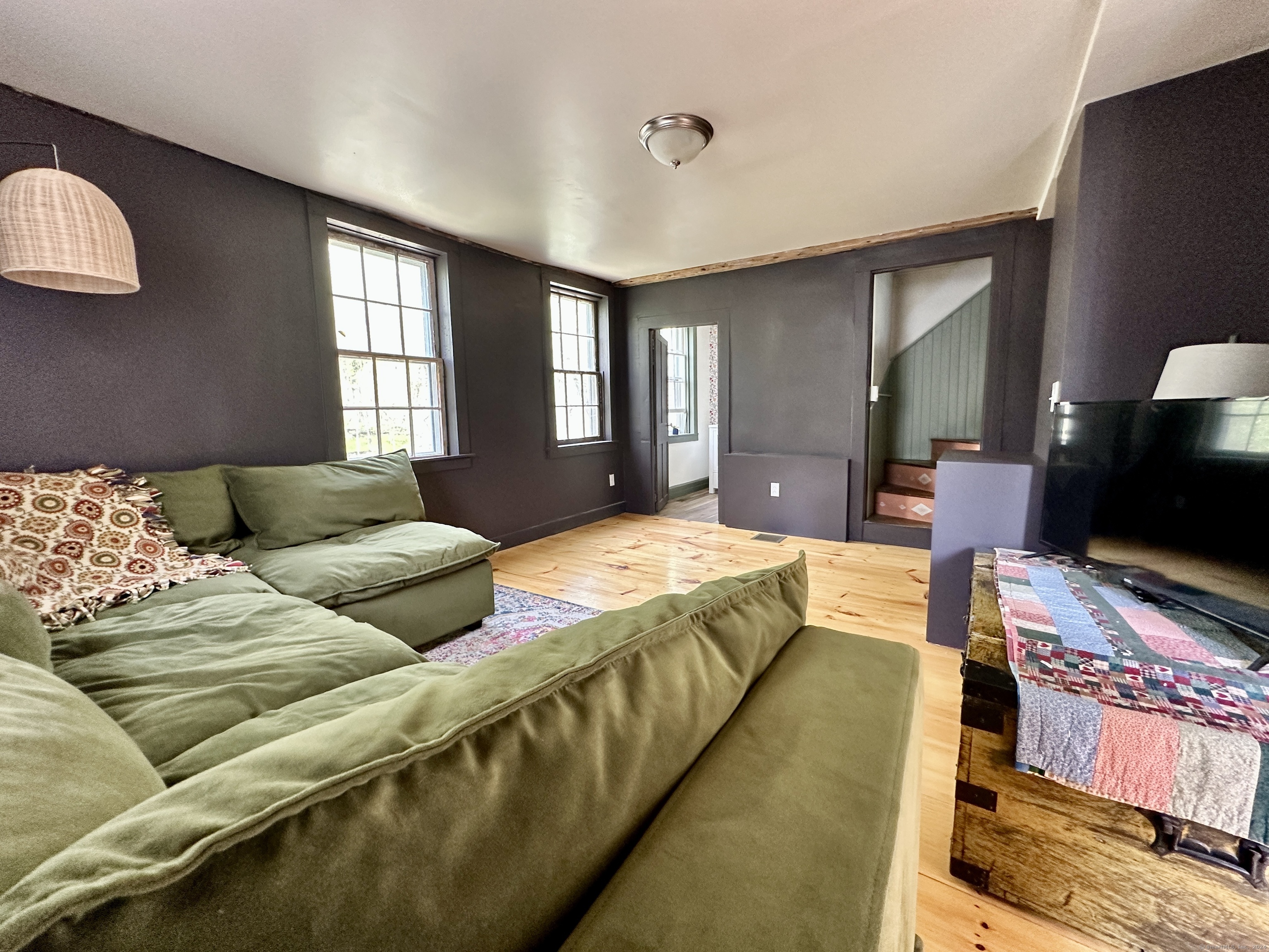 Living room with a green sectional, hardwood floors, tall windows, and a staircase.