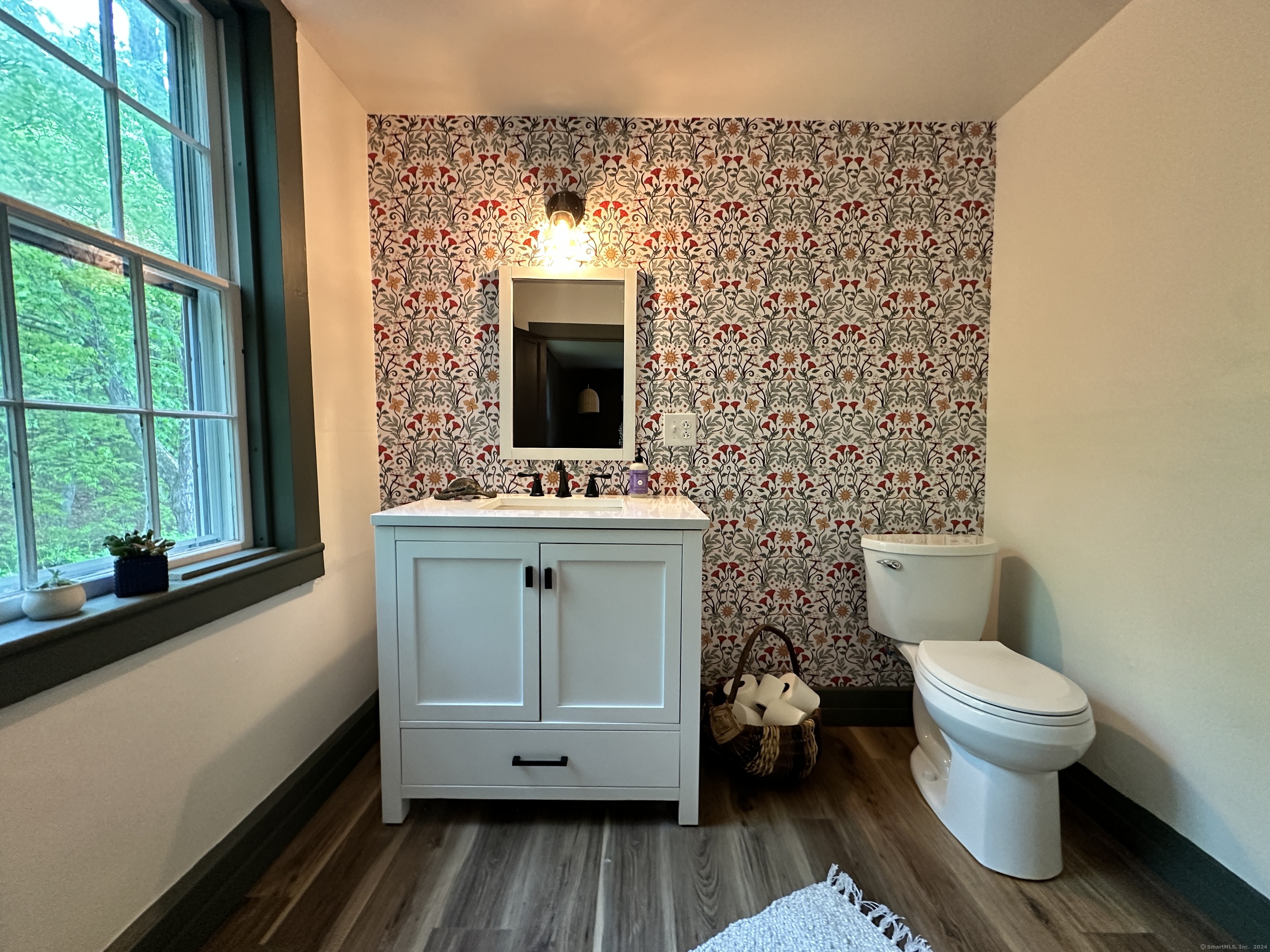 Bathroom with floral wallpaper, a white vanity, and a large window overlooking trees.