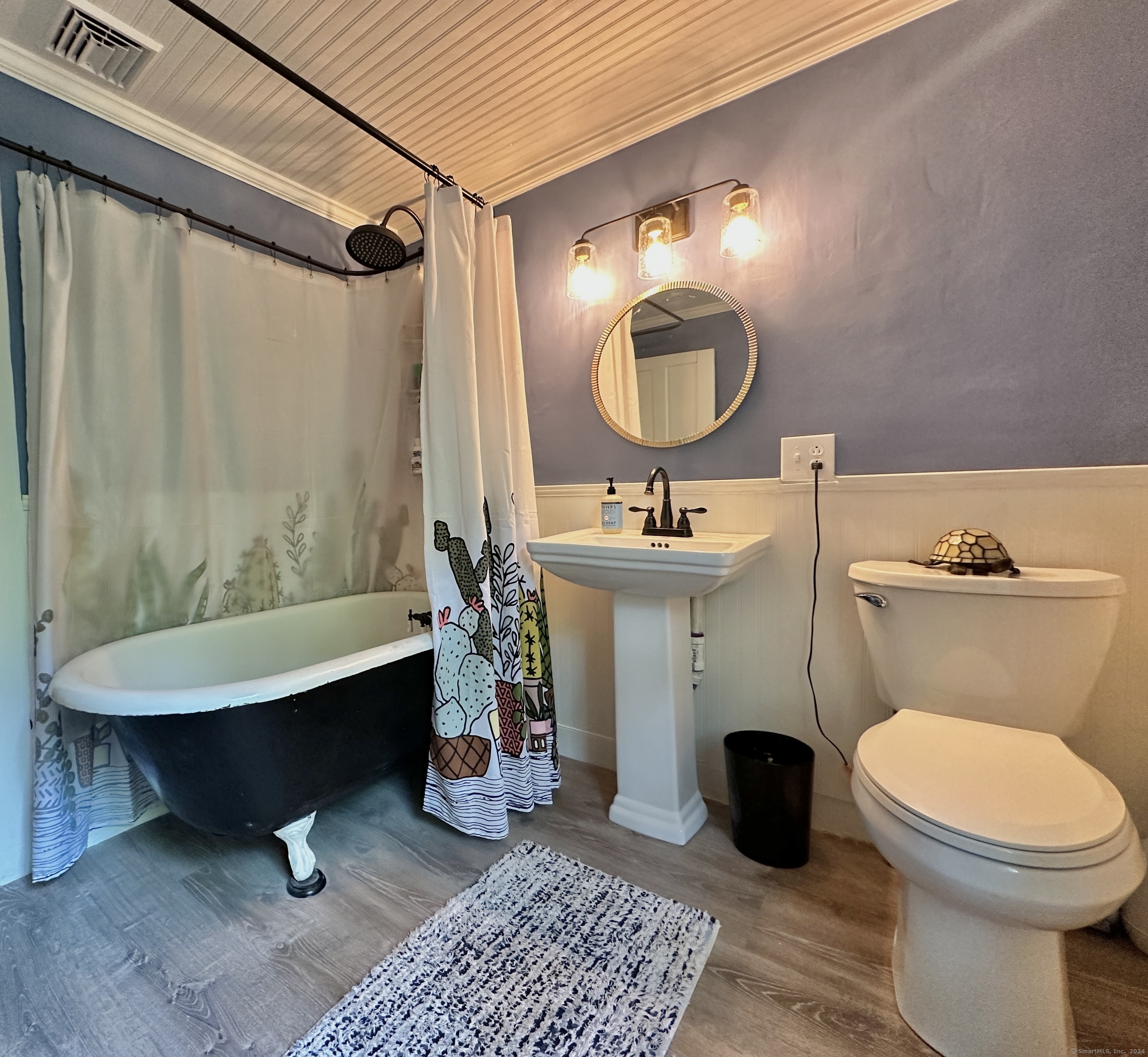 Bathroom with a black claw-foot tub, pedestal sink, and colorful cactus-print shower curtain.