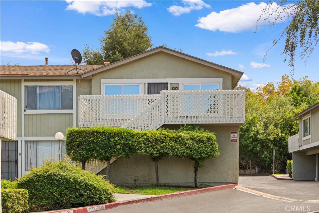 Two-story residential building with a raised white-lattice balcony and trimmed hedges.