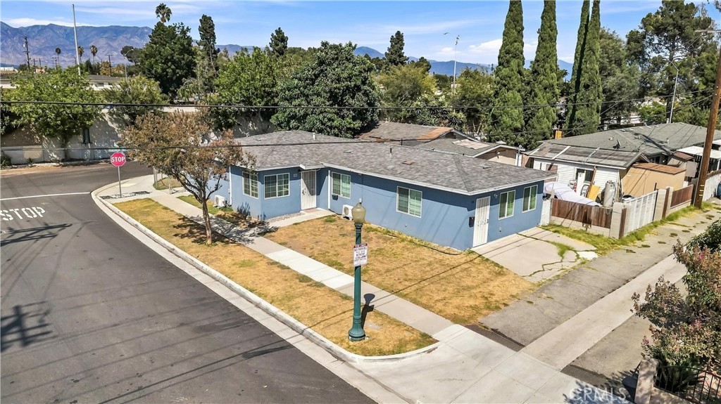 Blue single-story corner home with a dry lawn and mountains in the distance.