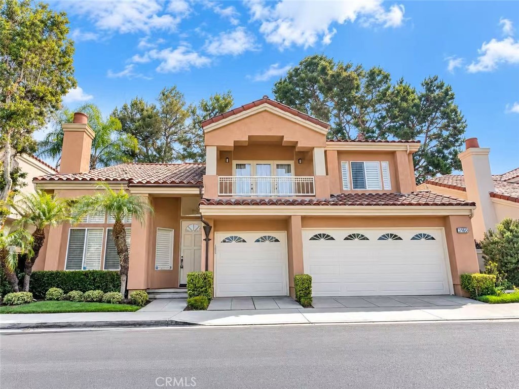 Two-story peach stucco home with a red tile roof, upper balcony, and two white garage doors.