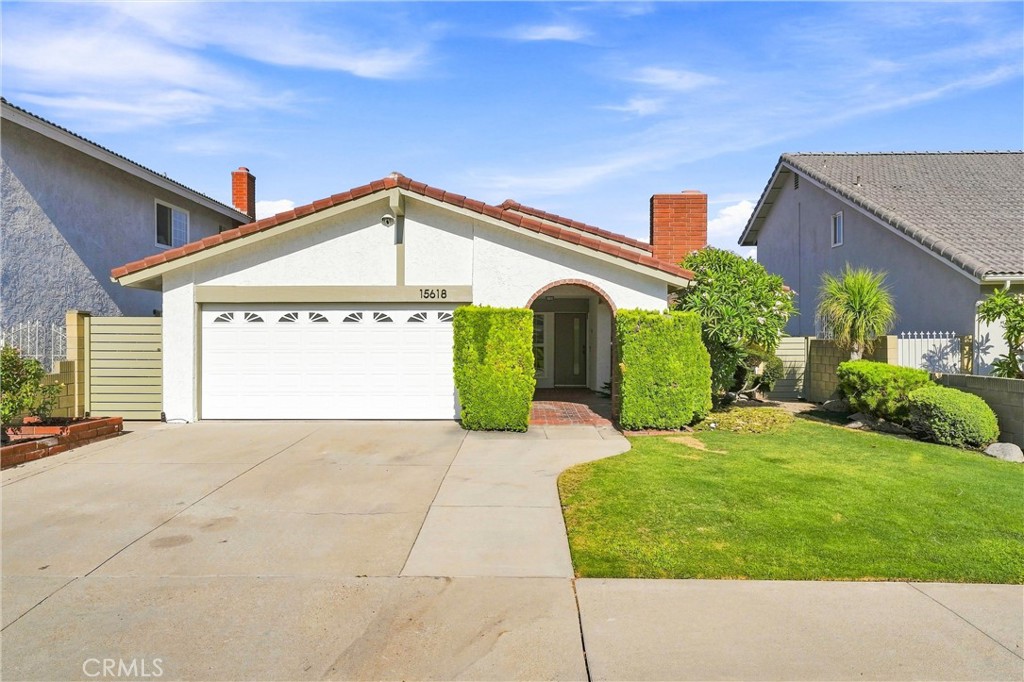 Single-story house with a red tile roof, arched entry, trimmed hedges, and wide driveway.