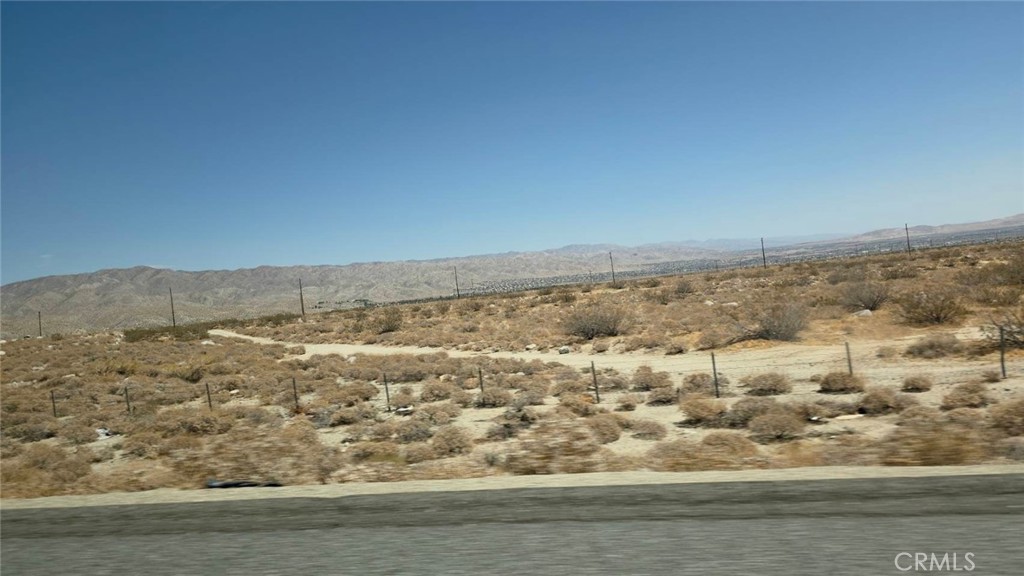 Desert land beside a paved road, with wire fencing and distant mountains.