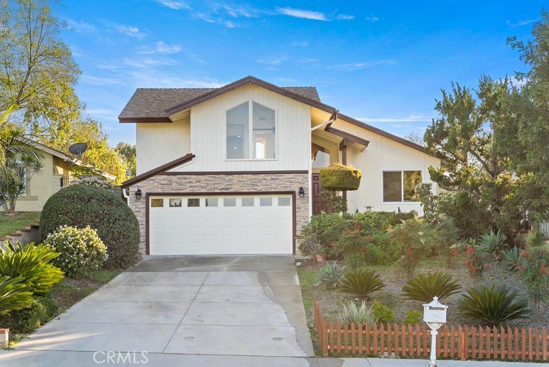 White two-story home with a double garage, concrete driveway, and landscaped front yard.