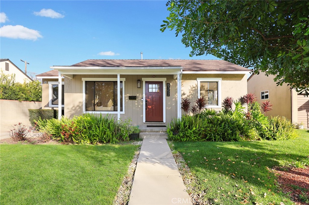 Single-story house with a red front door, landscaped garden beds, and a walkway across the lawn.
