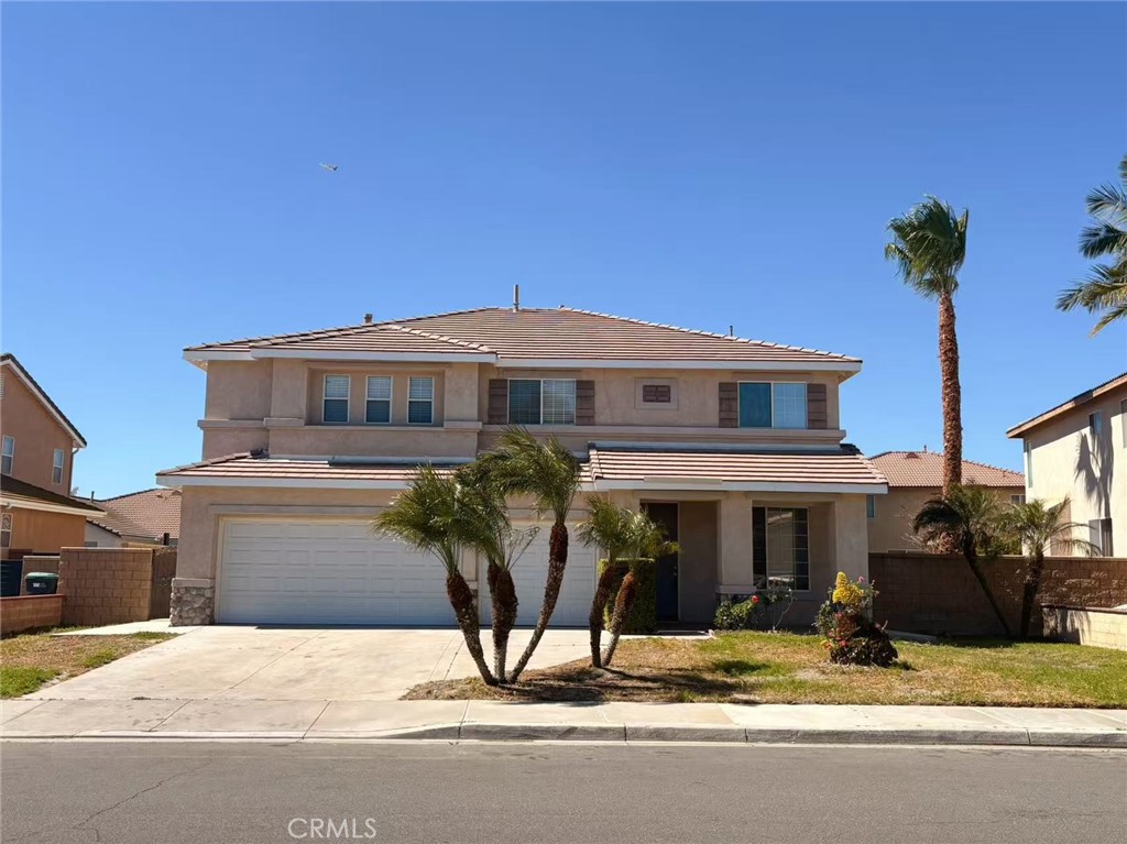 Two-story stucco home with a tiled roof, double garage, and palm trees.