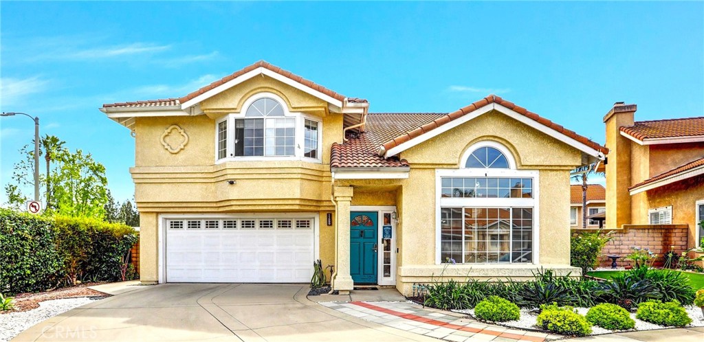 Yellow stucco house with arched windows, teal front door, and a wide driveway.