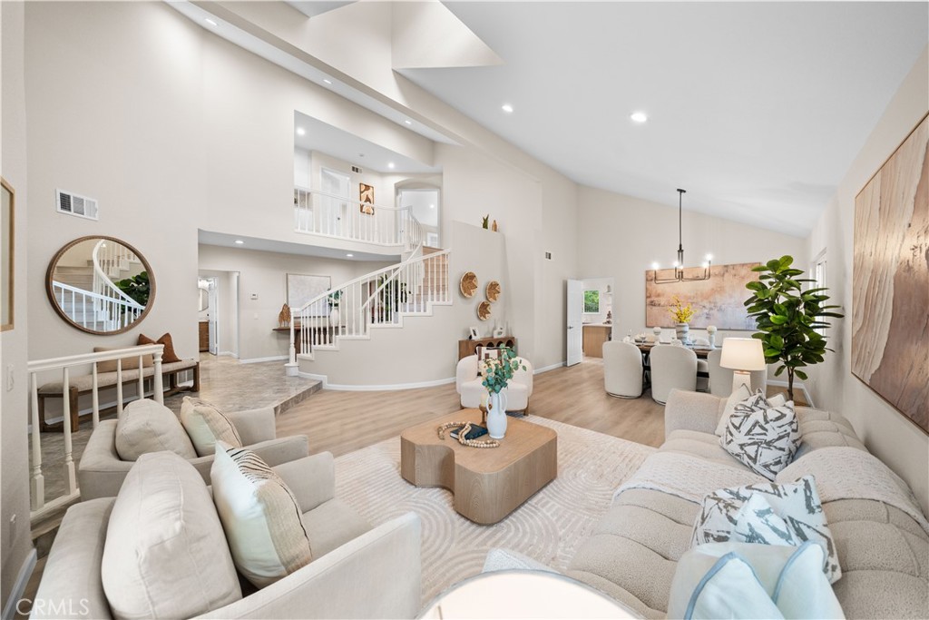 Open-plan living room with neutral sofas, a curved staircase and dining area.