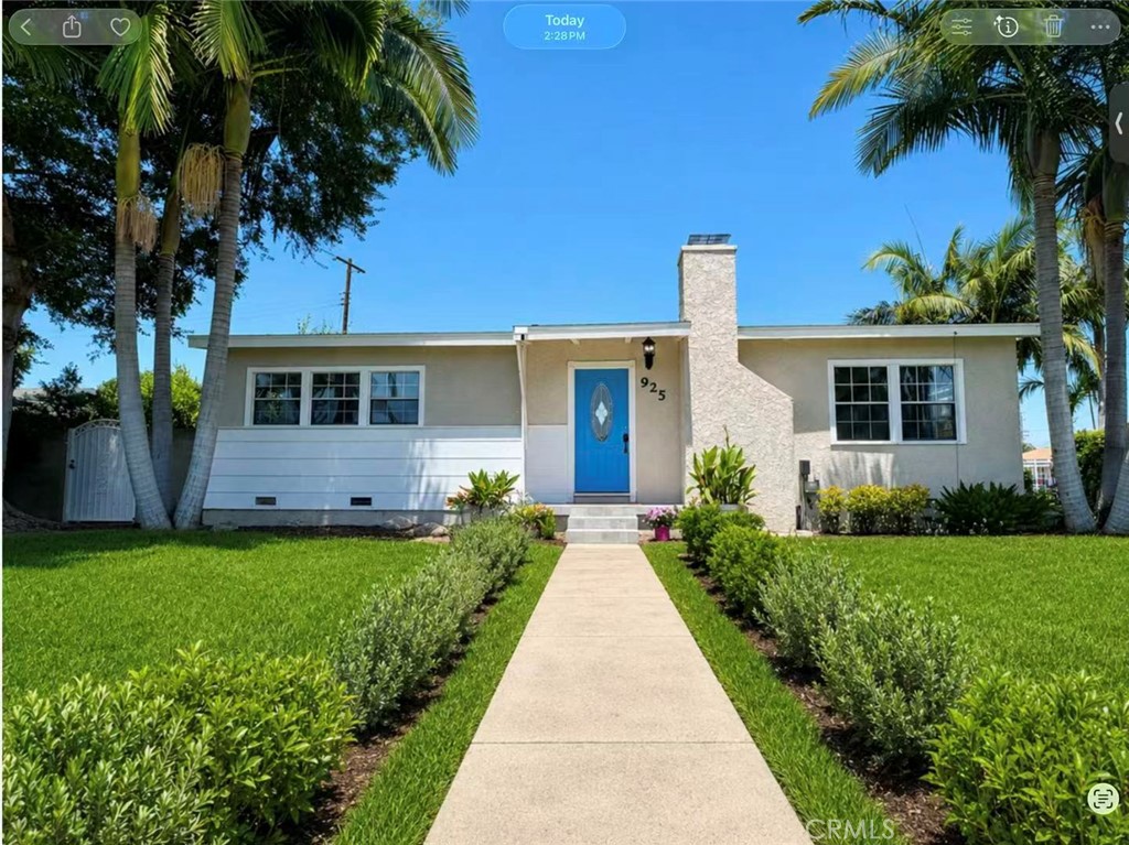 Single-story house with a bright blue front door, stone chimney, and palm-lined walkway.