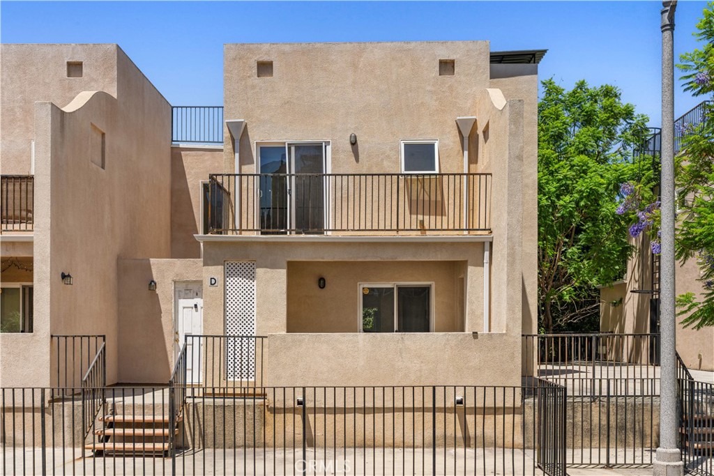 Beige two-story residence marked D, with black metal railings and an upper balcony.