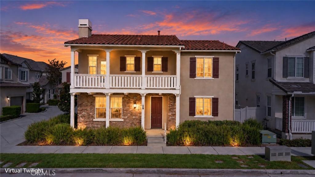 Two-story stucco home with a white balcony and warmly lit windows beneath a colorful dusk sky.