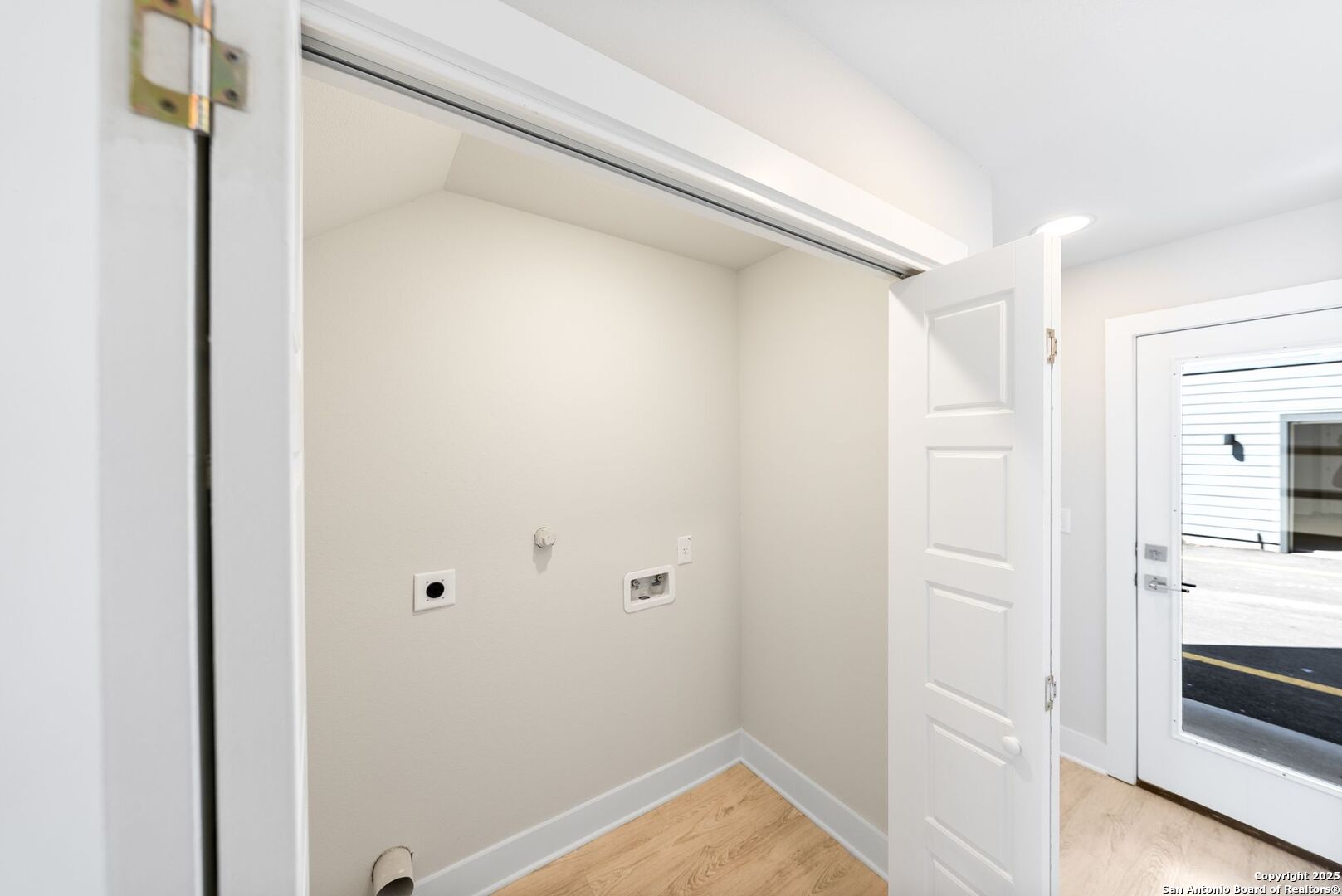 Empty laundry closet with washer and dryer hookups and light wood flooring.