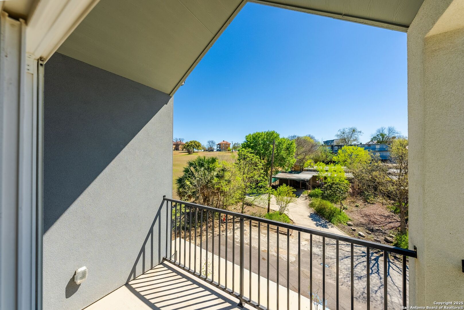 Apartment balcony overlooking landscaped grounds and nearby buildings.