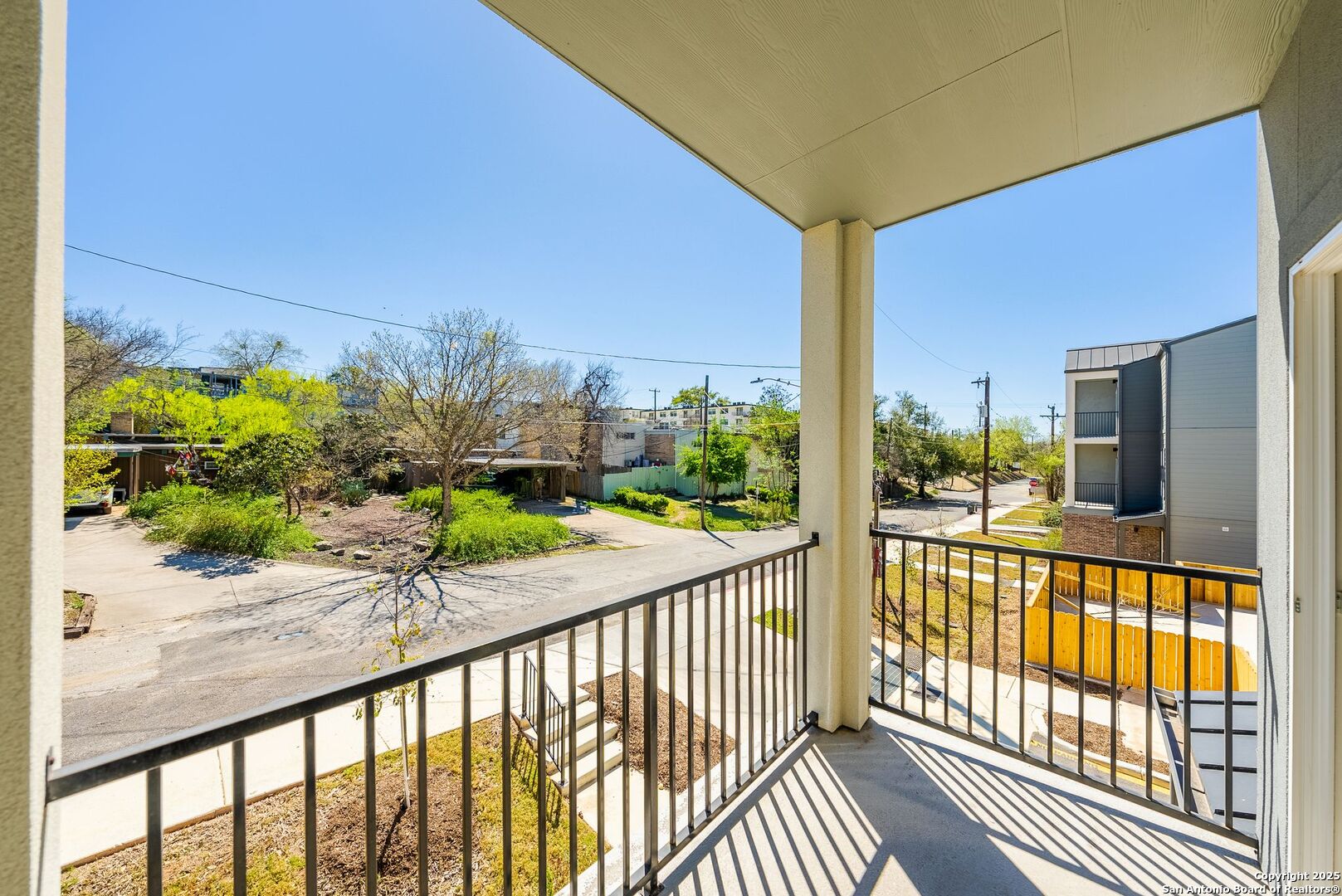 Covered balcony overlooking a tree-lined residential street and nearby buildings.