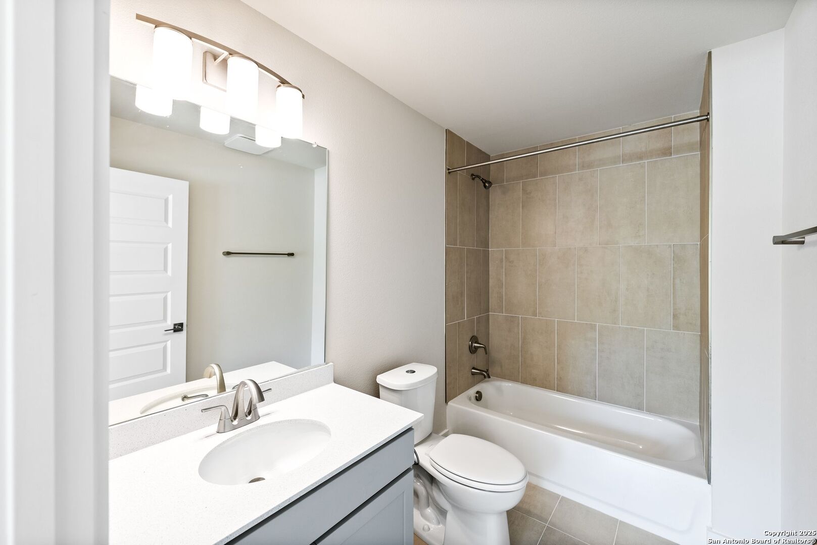 Bathroom with white vanity and large mirror beside a tub with beige tile surround.