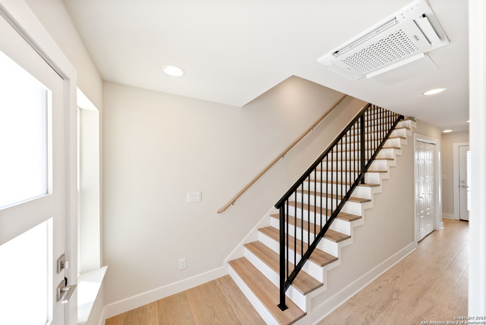 Entry hall staircase with wood treads, black railing, and light wood flooring.