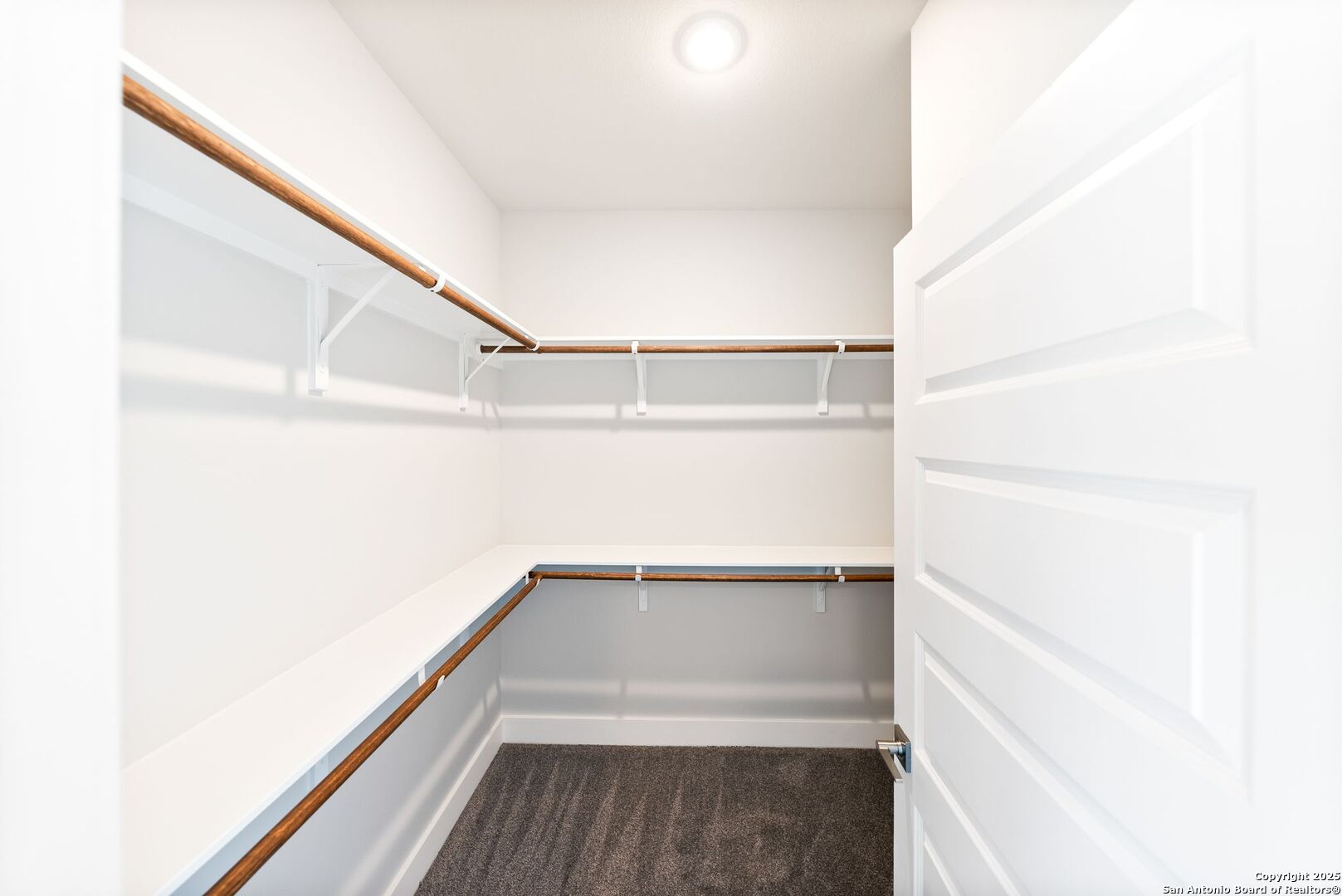 Walk-in closet with wraparound shelving, wood hanging rods, gray carpet, and an open white door.