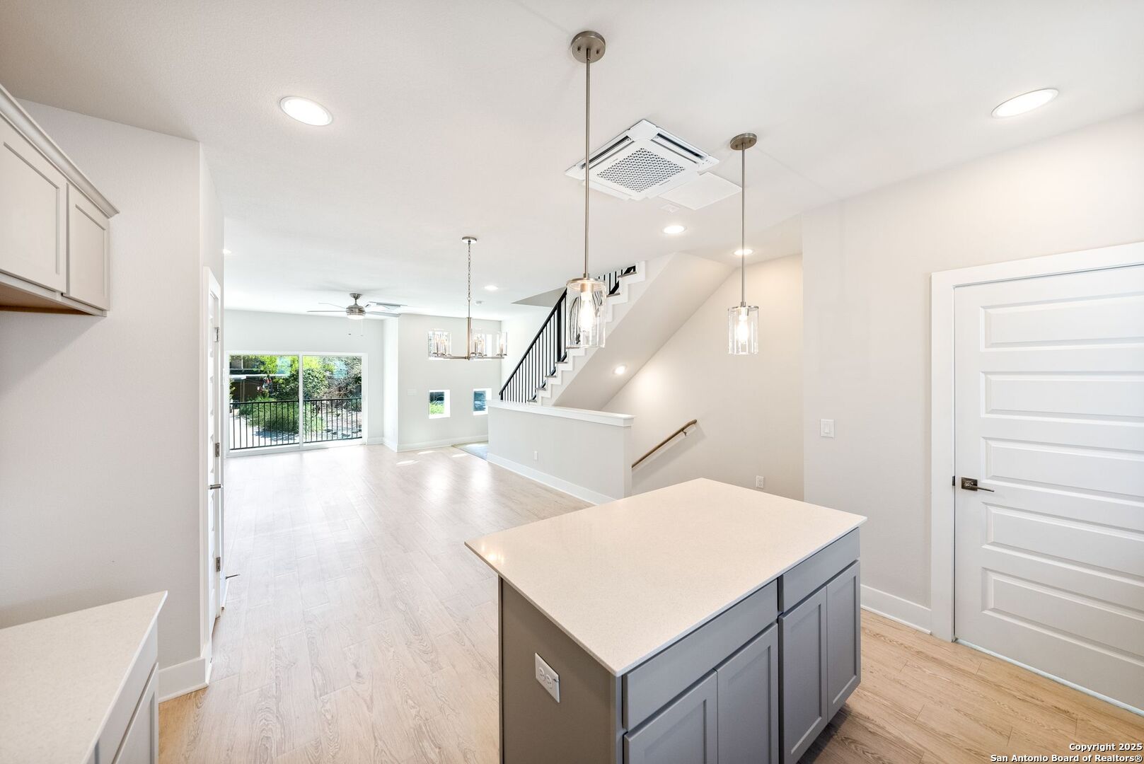 Unfurnished kitchen with a gray island, opening to a bright living area and staircase.