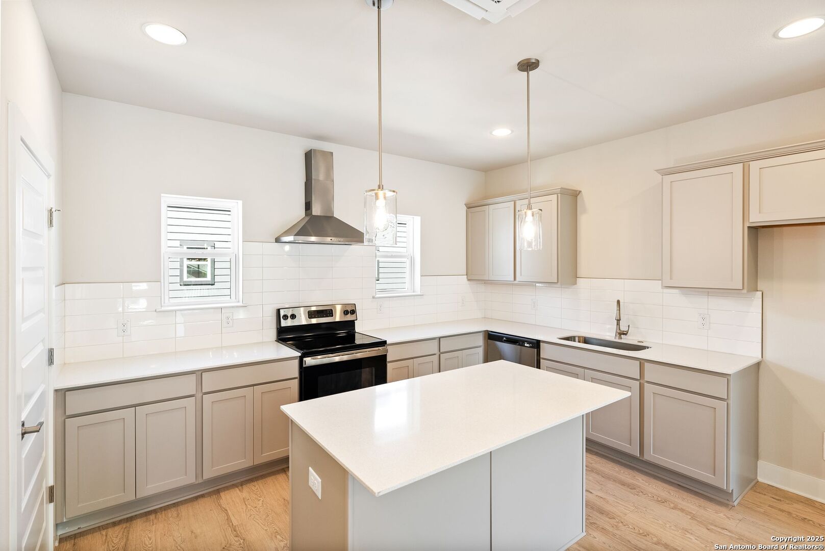 Vacant kitchen with a large island, taupe cabinets, white tile backsplash, and stainless steel range.