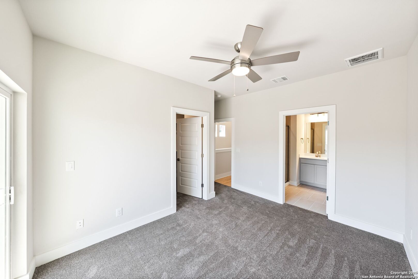 Vacant carpeted bedroom with a ceiling fan and an open doorway to the bathroom.