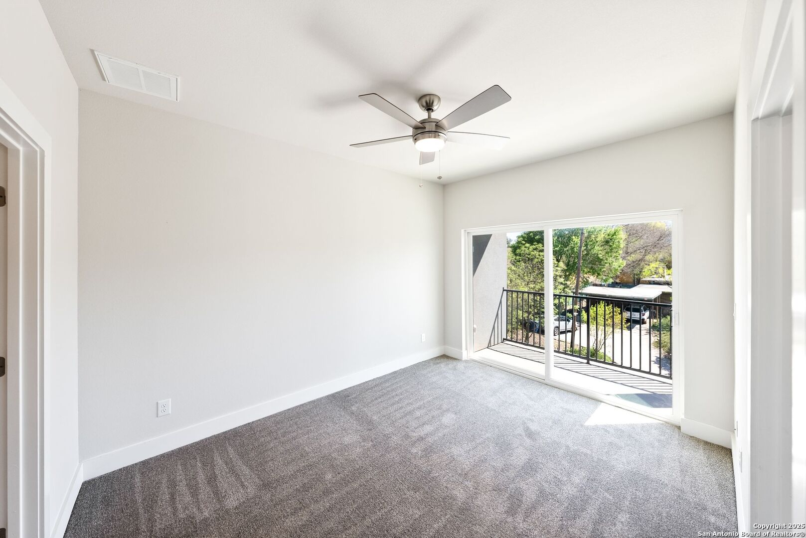 Empty carpeted bedroom with a ceiling fan and sliding glass doors opening to a balcony.