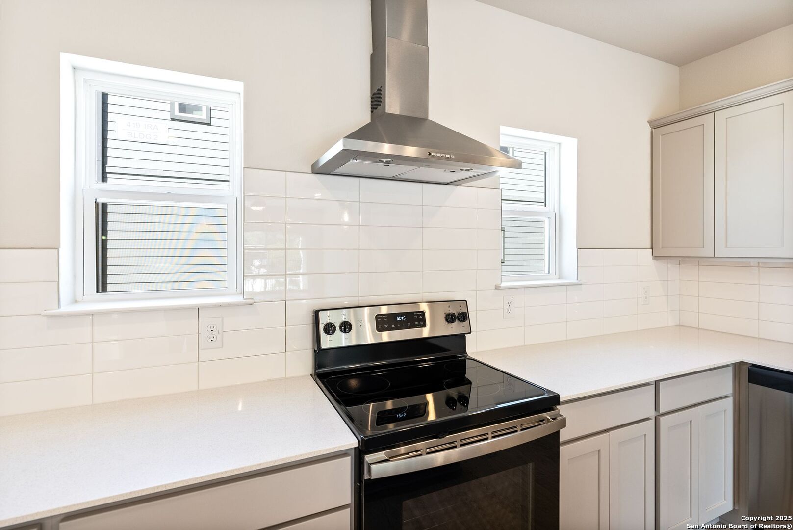 Bright kitchen with white cabinetry, glossy tile backsplash, and a black-and-stainless electric range.