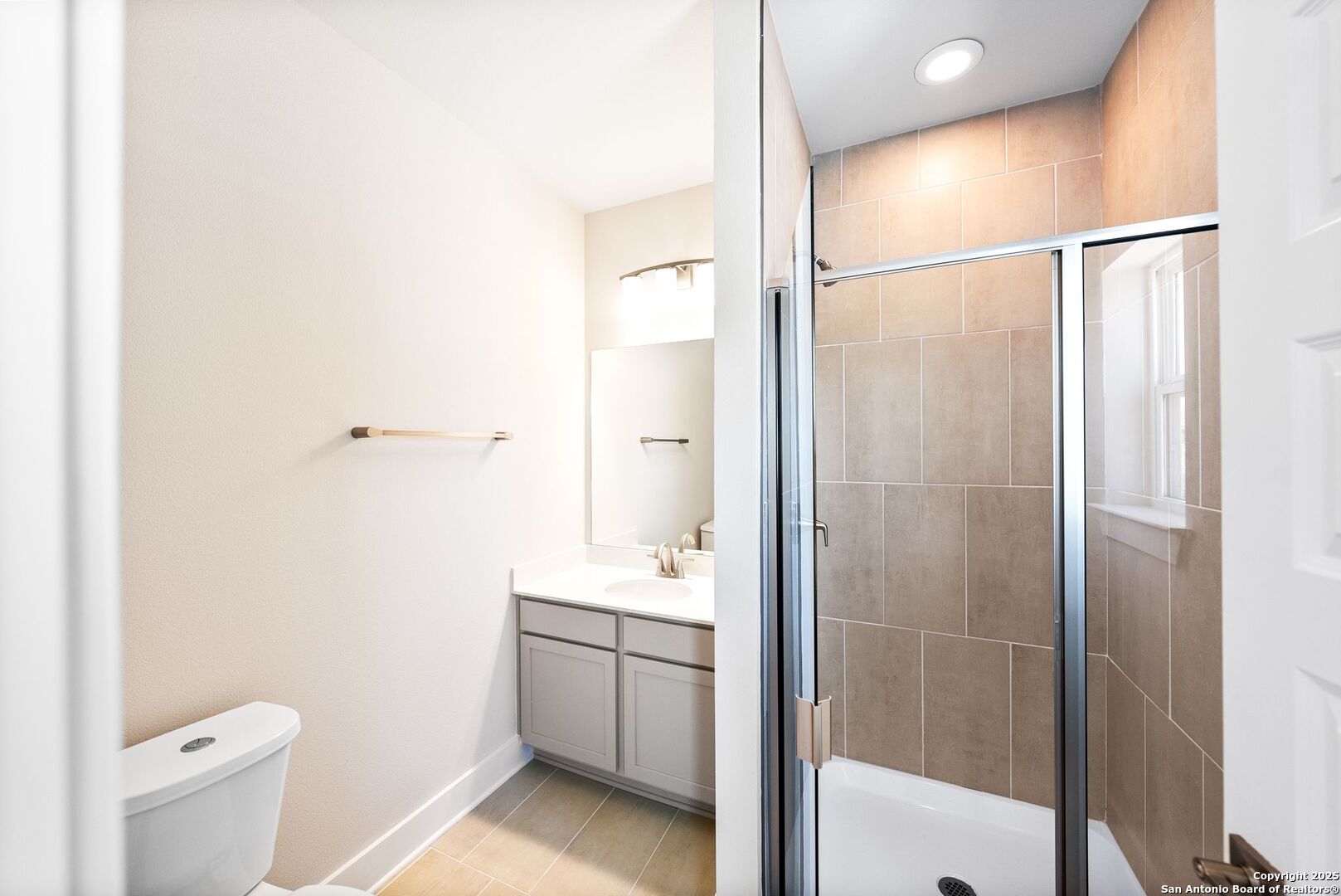 Bathroom with a glass-enclosed, beige-tiled tub-shower beside a white vanity.