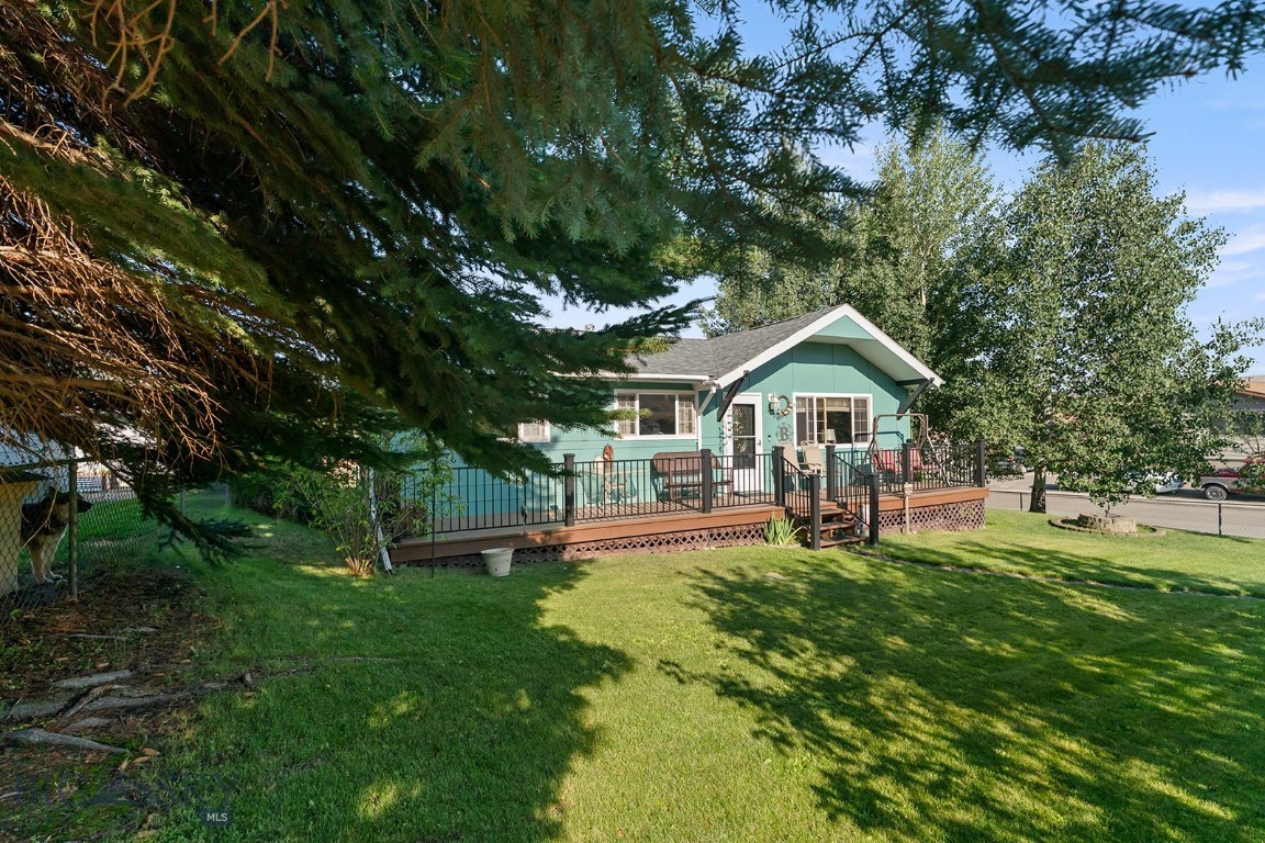 Turquoise house with a raised deck and black railing beneath mature trees.